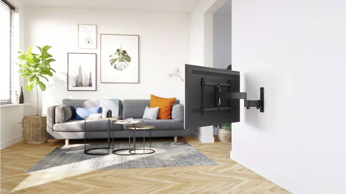 Een woonkamer met een bank, kussens en een tv-beugel aan de muur. Planten en wandkunst zorgen voor een gezellige sfeer.