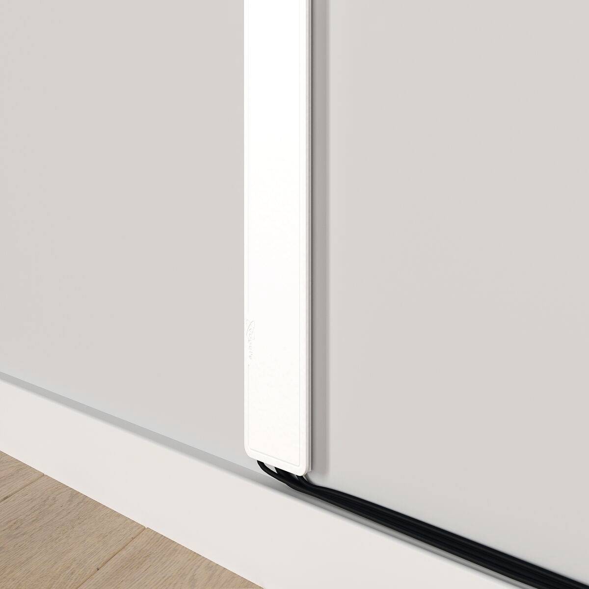 Een witte kabelgoot is verticaal gemonteerd aan een grijze muur. Een zwart kabel loopt langs de bodem van de goot.