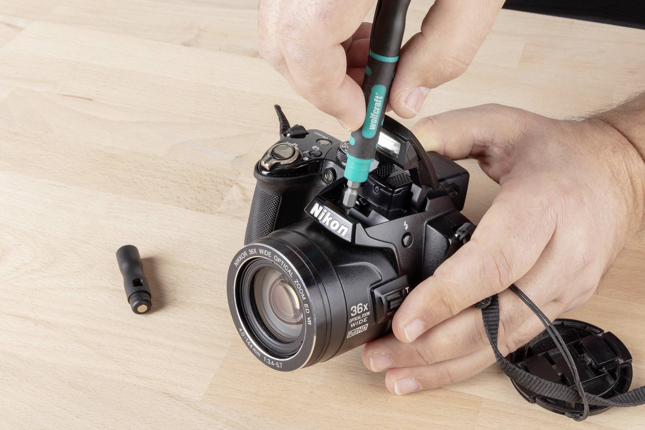 Een persoon reinigt de lens van een Nikon-camera met een speciale reinigingsstift op een houten tafel.