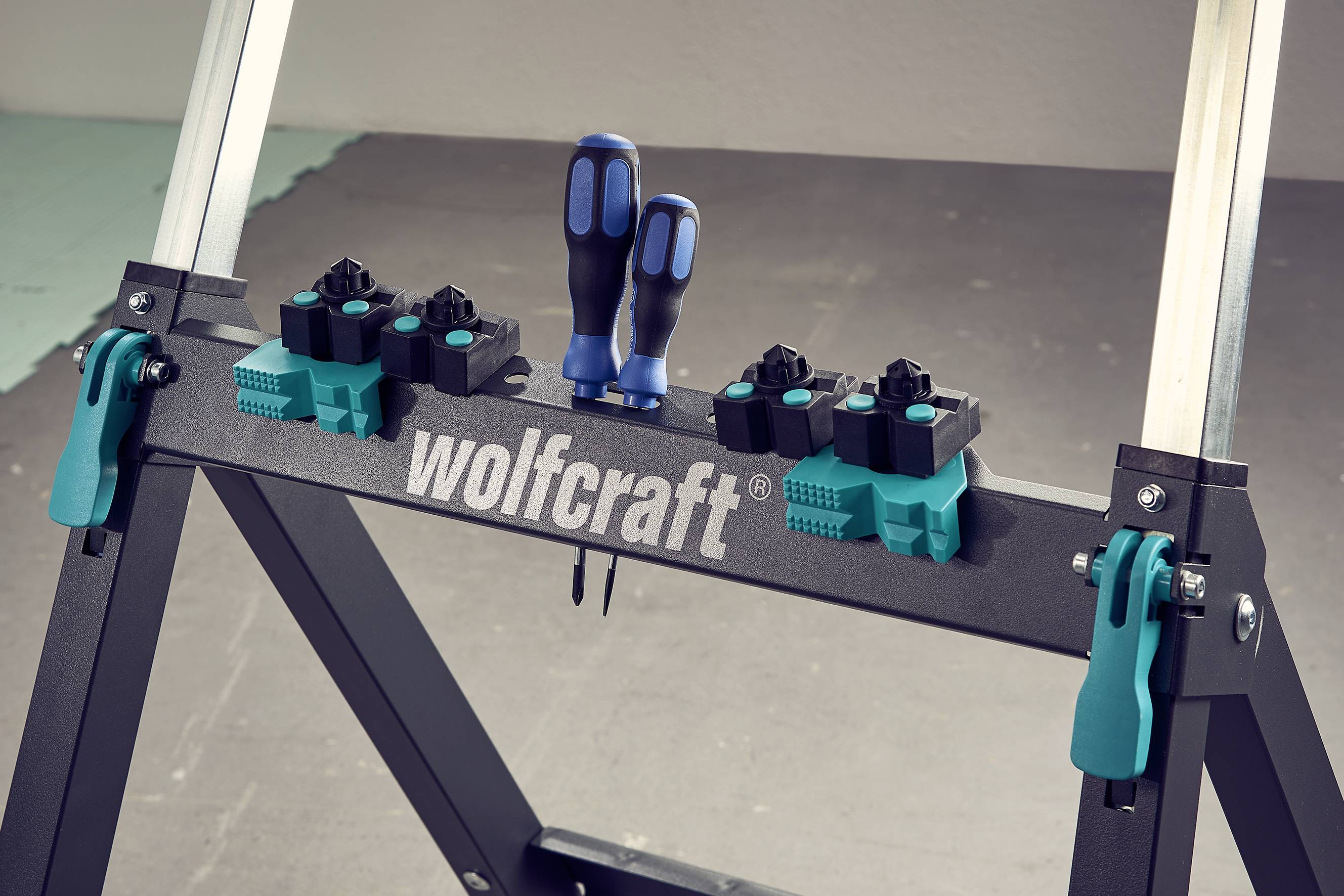 Een werkbank van 'wolfcraft' met gereedschapshouders en twee schroevendraaiers in blauw en zwart, op een grijze achtergrond.