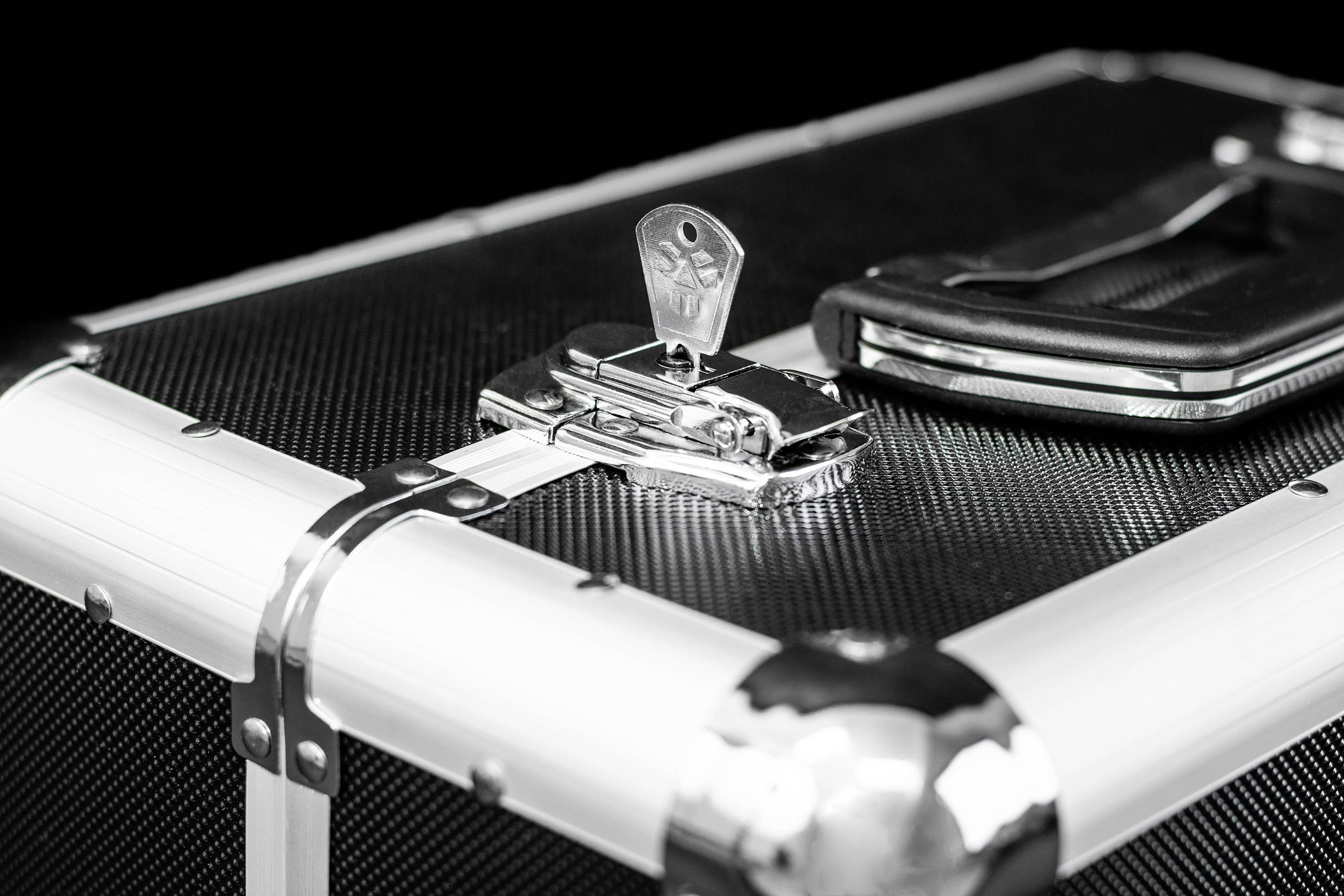 Zwarte koffer met een zilveren slot en sleutel, waarop een zwart etui ligt.