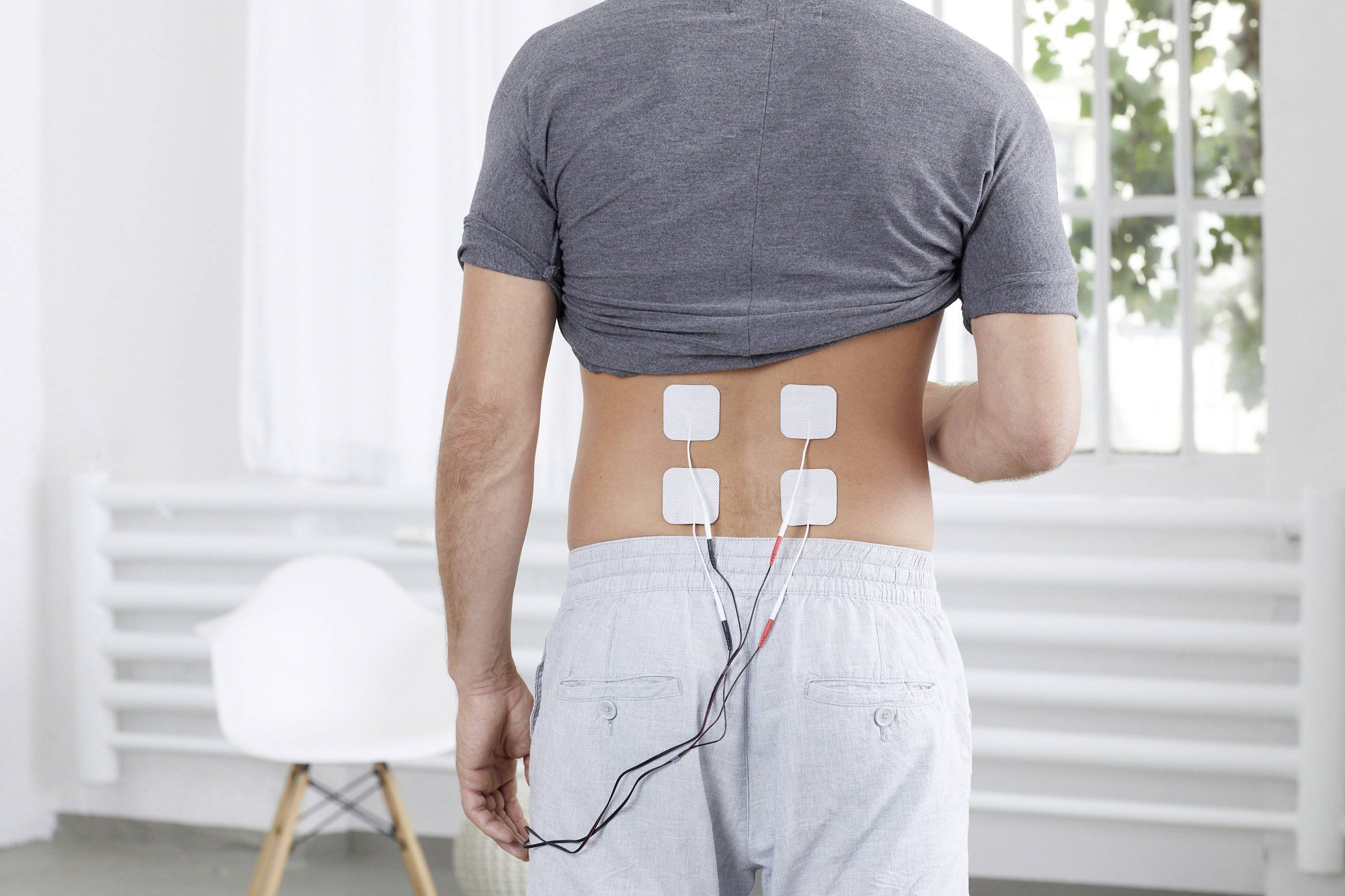 Een man met blote rug staat in een ruimte met medische elektroden op zijn onderrug geplaatst.