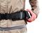 Een persoon doet een zwarte riem met metalen gesp om. De kleding is beige, de achtergrond wit.