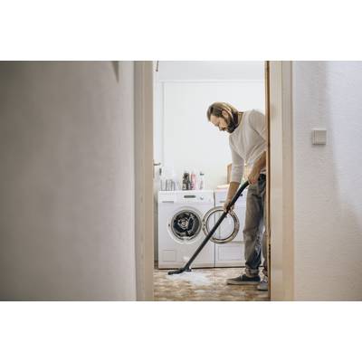 Een persoon die de vloer van een wasruimte stofzuigt, naast een wasmachine en droger.
