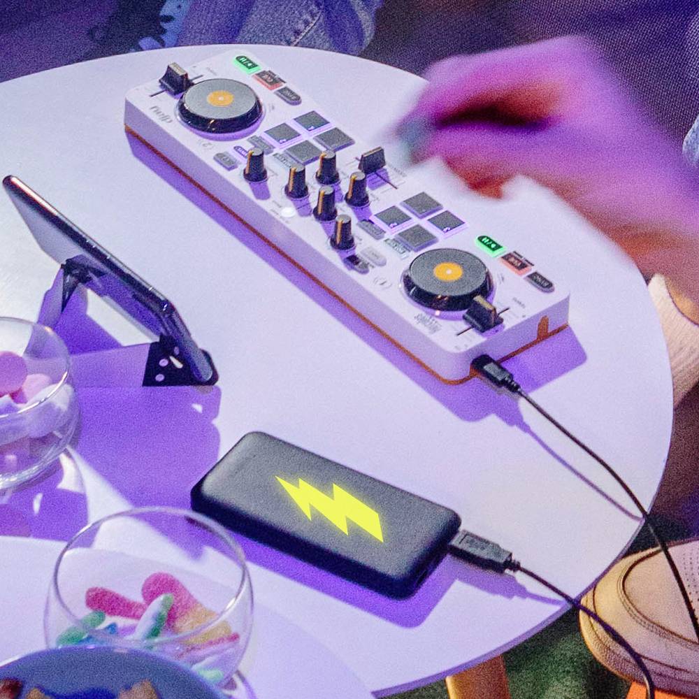 Een persoon bedient een kleine mengconsole op een tafel, met een mobiele telefoonhouder en een schaal vol snoepgoed.