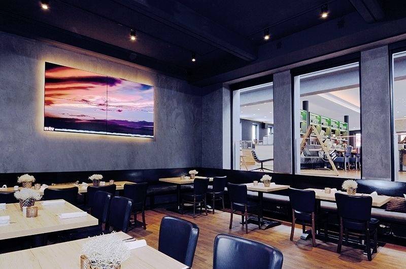 Een modern restaurant met houten vloeren, zwarte stoelen en tafels. Een groot schilderij toont een kleurrijke zonsondergang aan de muur.
