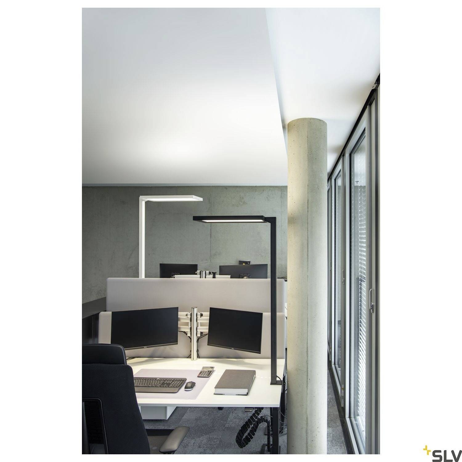 Lichte, moderne kantoorruimte met twee computermonitoren op een bureau, omgeven door grijze muren en grote ramen.