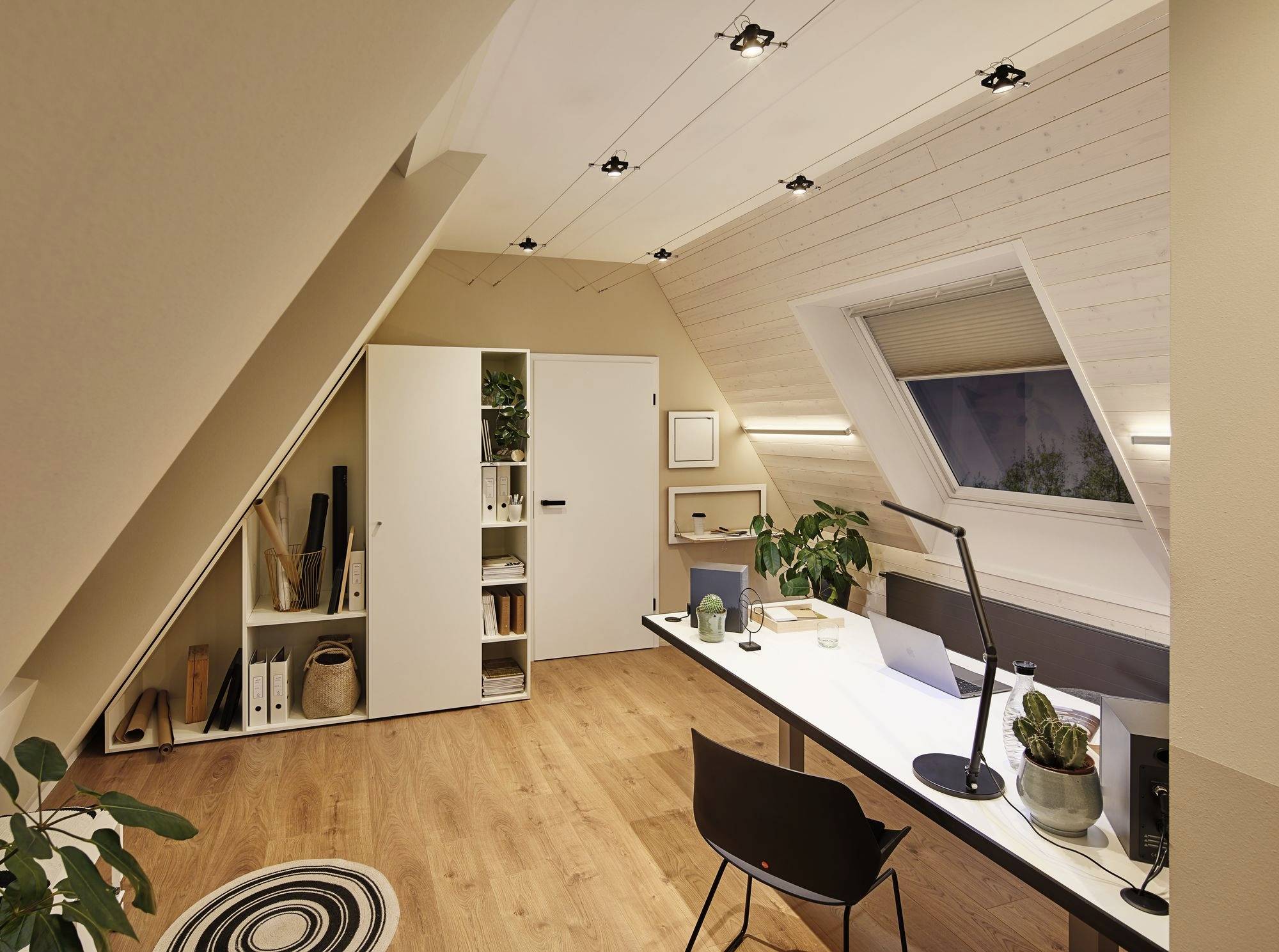 Een modern, goed verlicht zolderkantoor met houten vloer. Een lange tafel met laptop en planten. Rek met mappen.