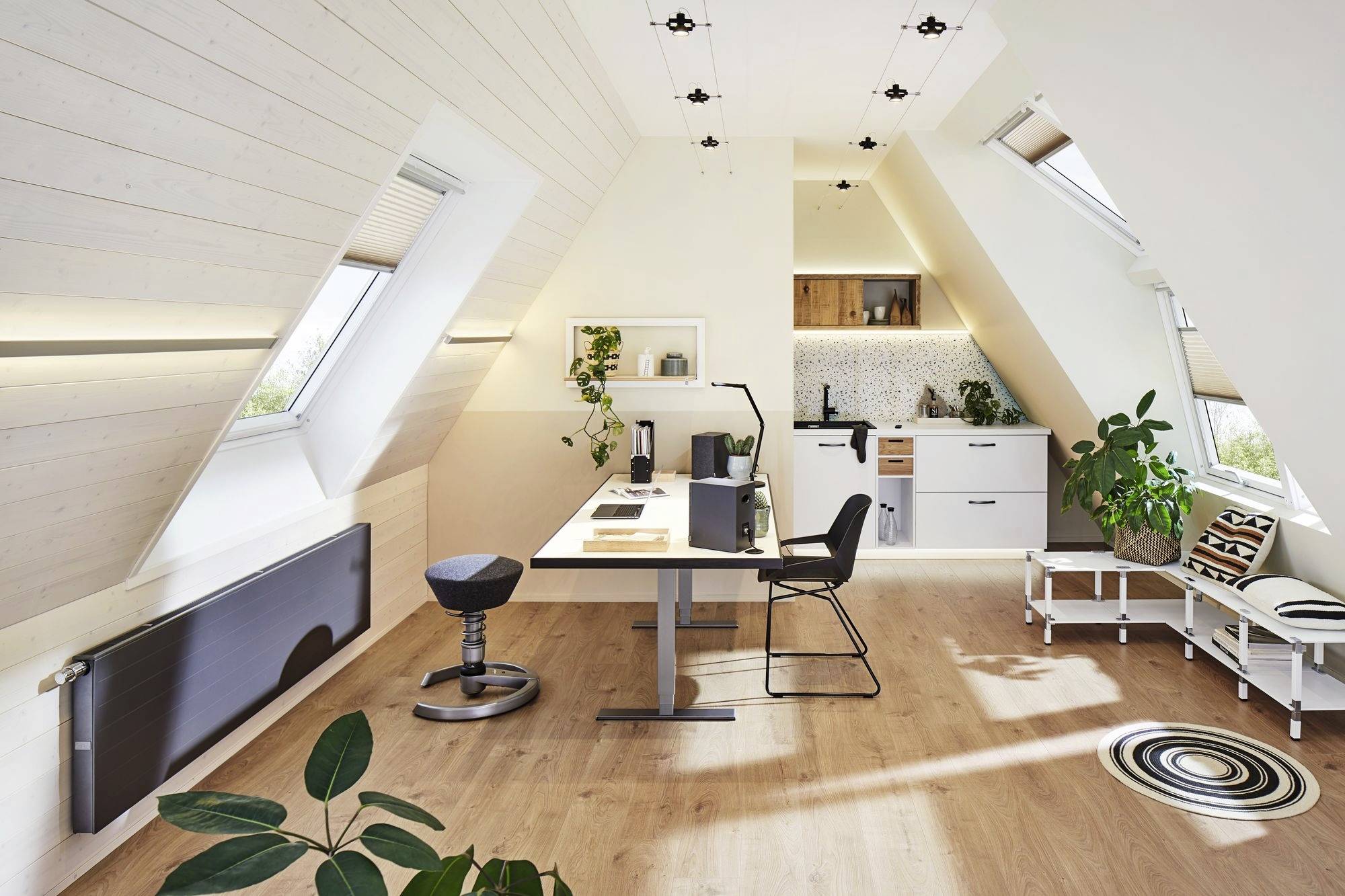 Een modern, licht overspoeld zolderkantoor met een bureau, stoel, planten en een kleine kitchenette op de achtergrond.