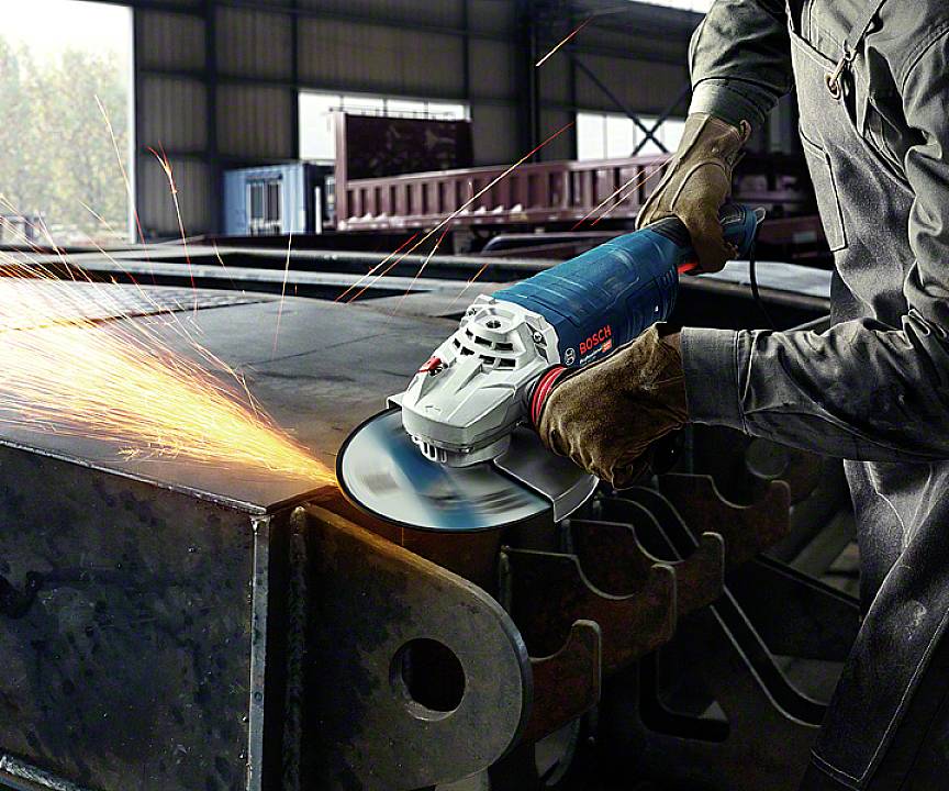 Een arbeider gebruikt een blauwe slijpmachine, vonken spatten rond. Scène in een fabriekshal, metaalbewerking.