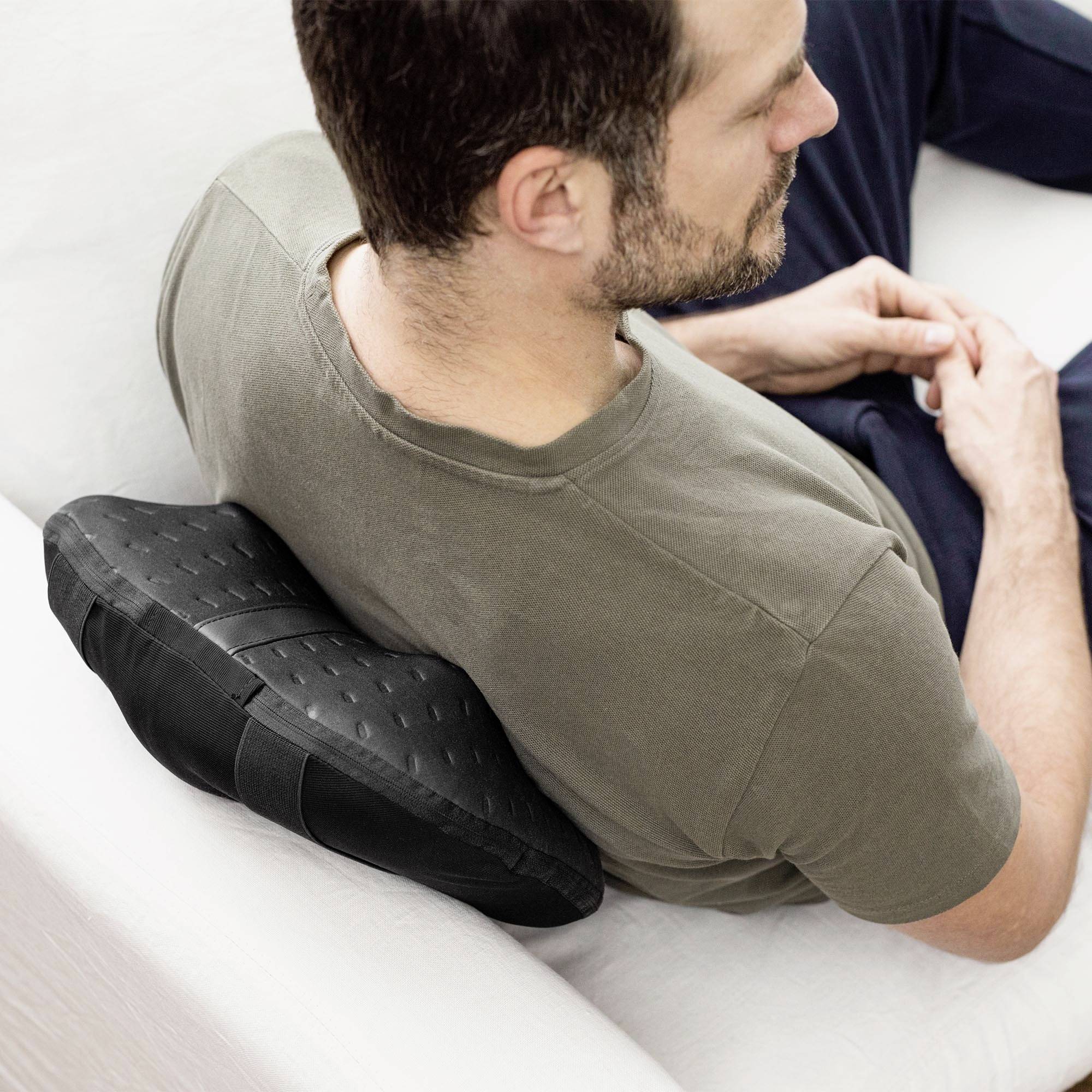 Een zittende persoon gebruikt een ergonomisch kussen op een bank. Het kussen ondersteunt de rug voor meer comfort.