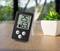 Digitale thermometer en hygrometer op een tafel tonen 25°C en 63% luchtvochtigheid. Op de achtergrond staat een plant.