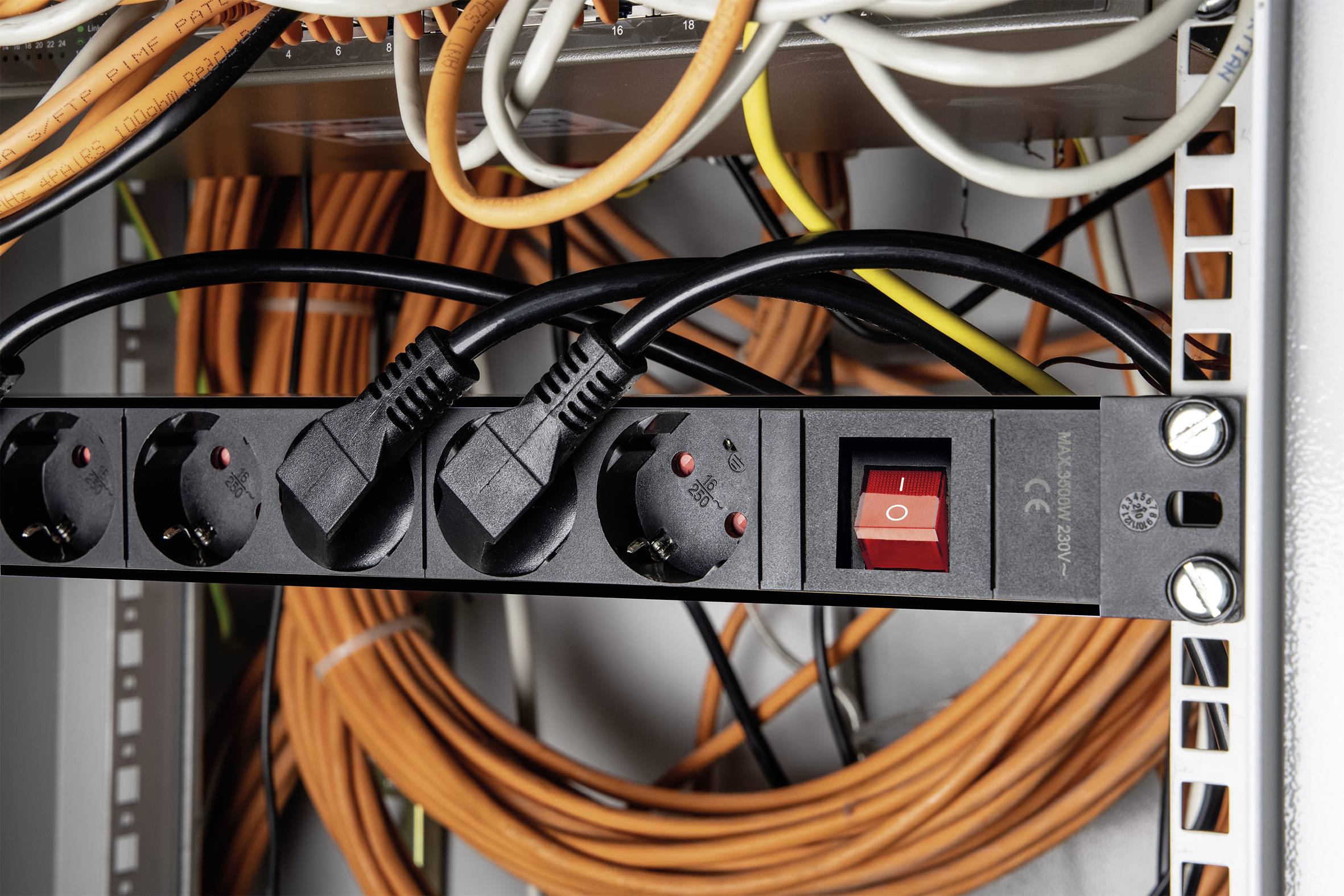 Een netwerk-serverrek toont drie netstekkers die zijn aangesloten op een stekkerdoos. Op de achtergrond lopen oranje kabels.