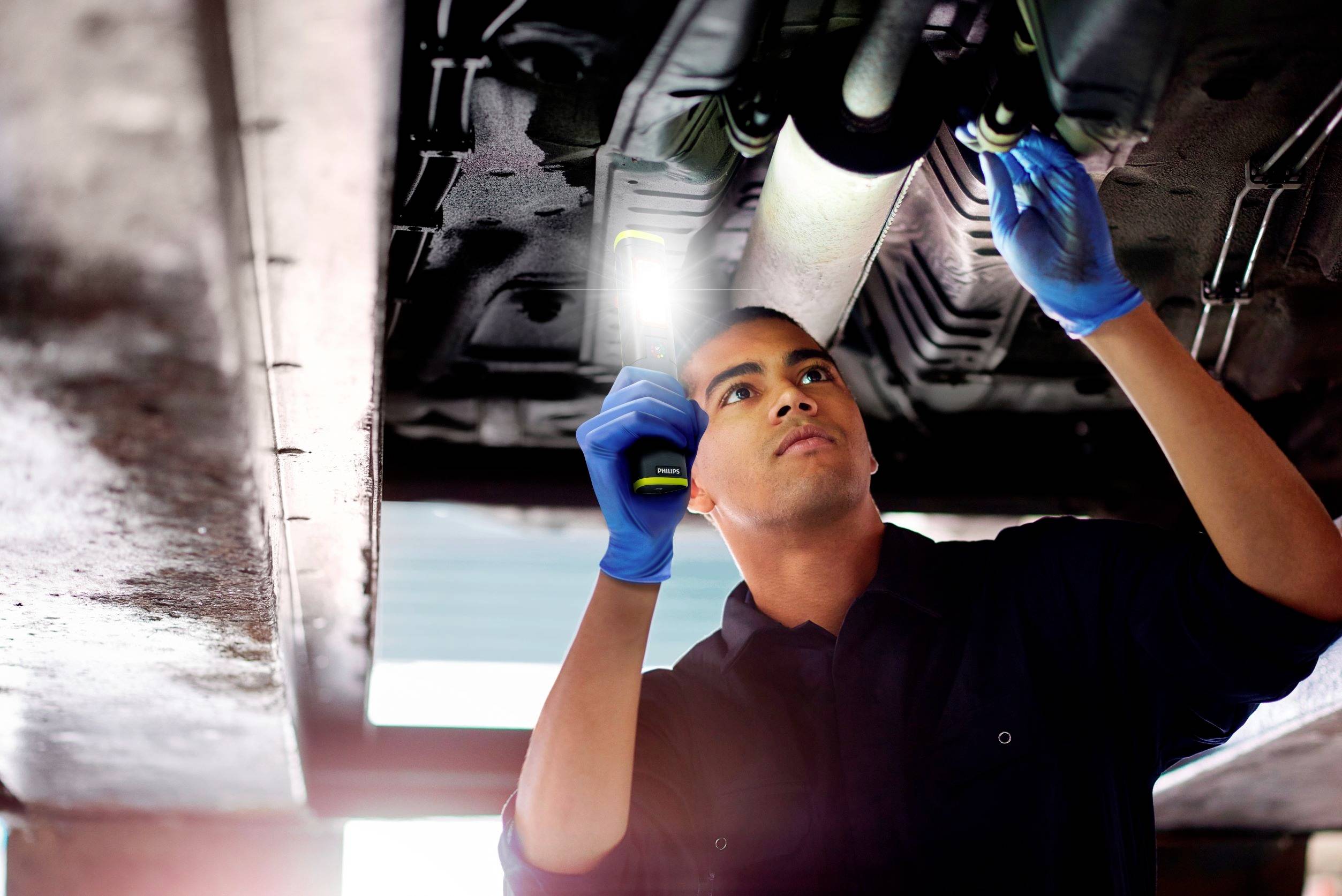 Een monteur werkt onder een auto en gebruikt een zaklamp om onderdelen te inspecteren.