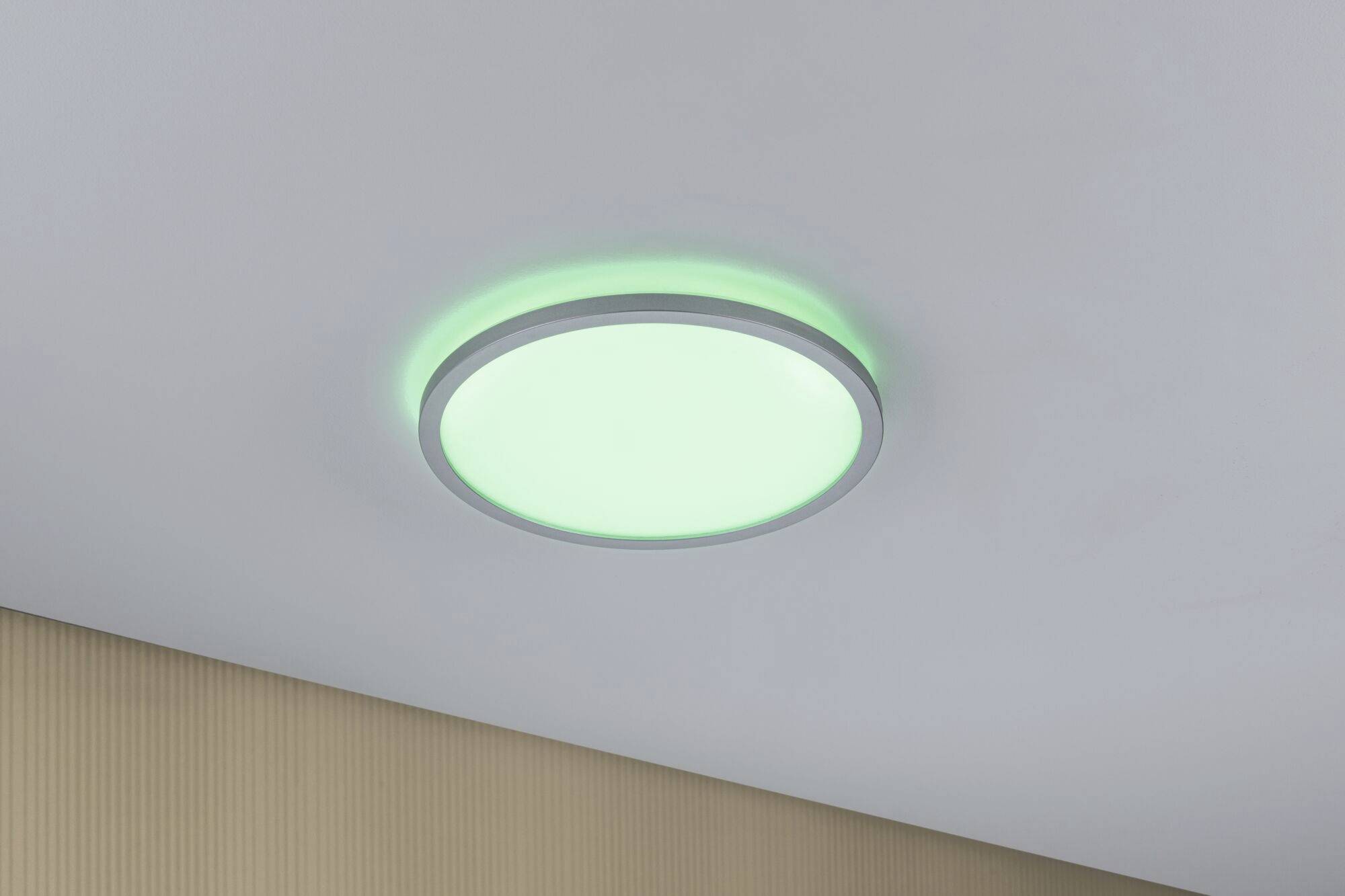 Een ronde LED-plafondlamp met groen licht aan het witte plafond van een kamer. Op de achtergrond is een beige behang zichtbaar.