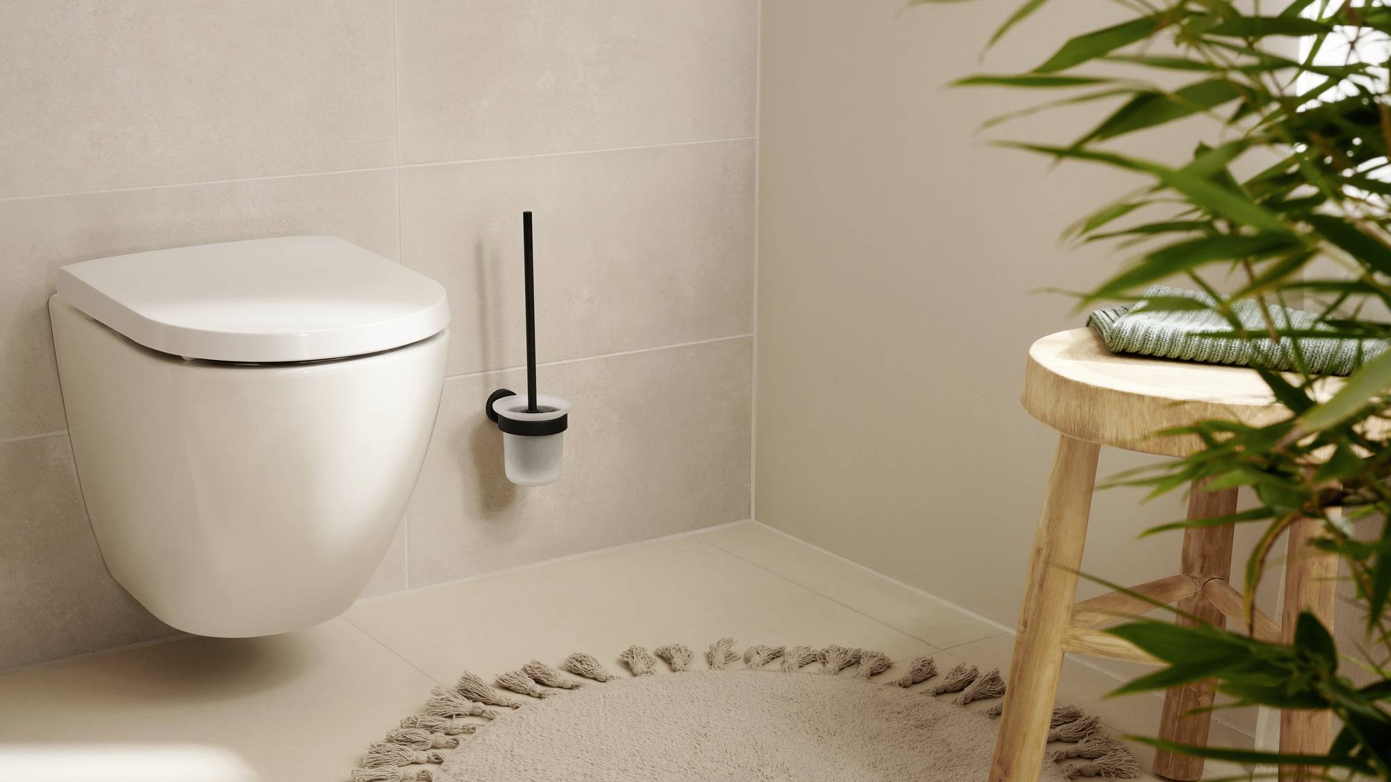 Een modern badkamer met een wit wandtoilet, een toiletborstel ernaast, een houten kruk en een bloemschikking.