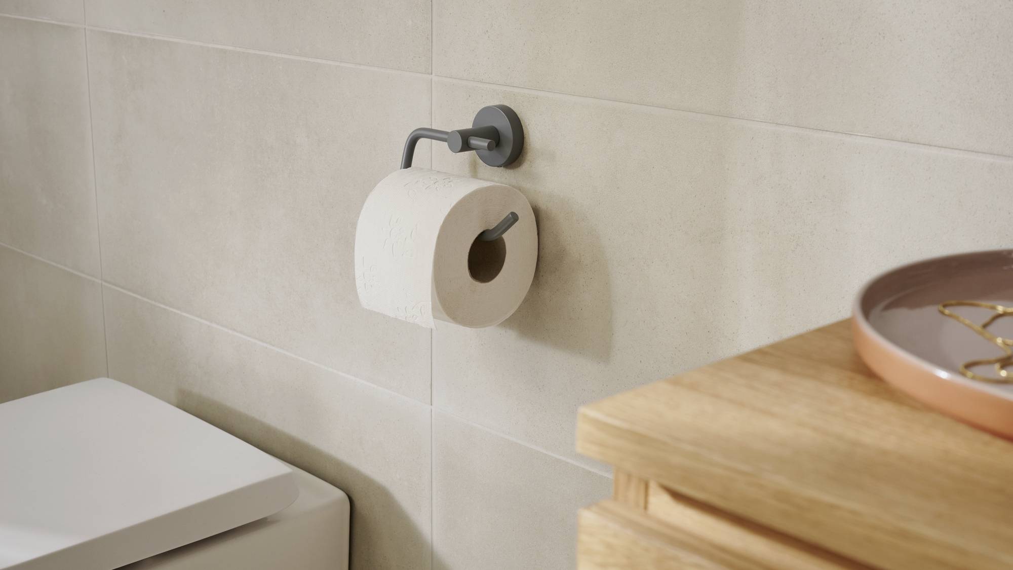 Rol toiletpapier aan de wandhouder in de badkamer naast een witte toiletbril en een houten plankje met decoratie.