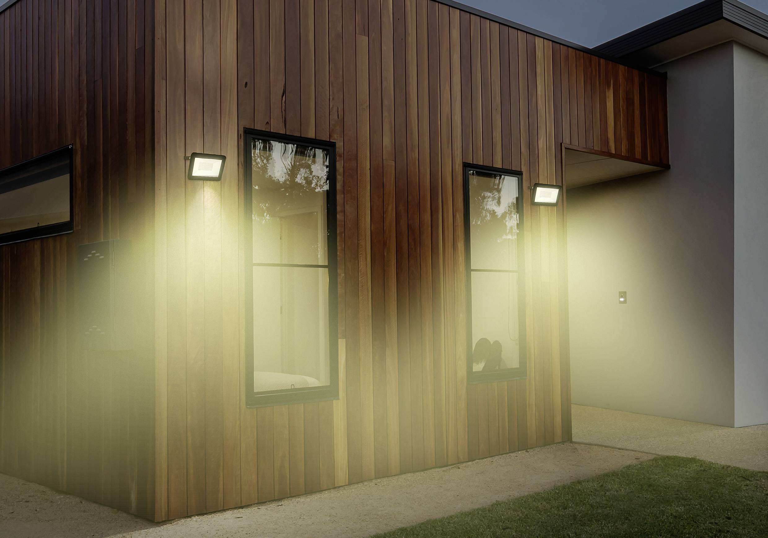 Een modern houten huis met ingeschakelde buitenverlichting bij het invallen van de avond. Eenvoudige architectuur met strakke lijnen en glasgevels.