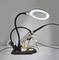 Een vergrootlamp met een verstelbare arm is verlicht en gepositioneerd boven een soldeerstations uitgerust met gereedschaphouders en soldeeraccessoires.