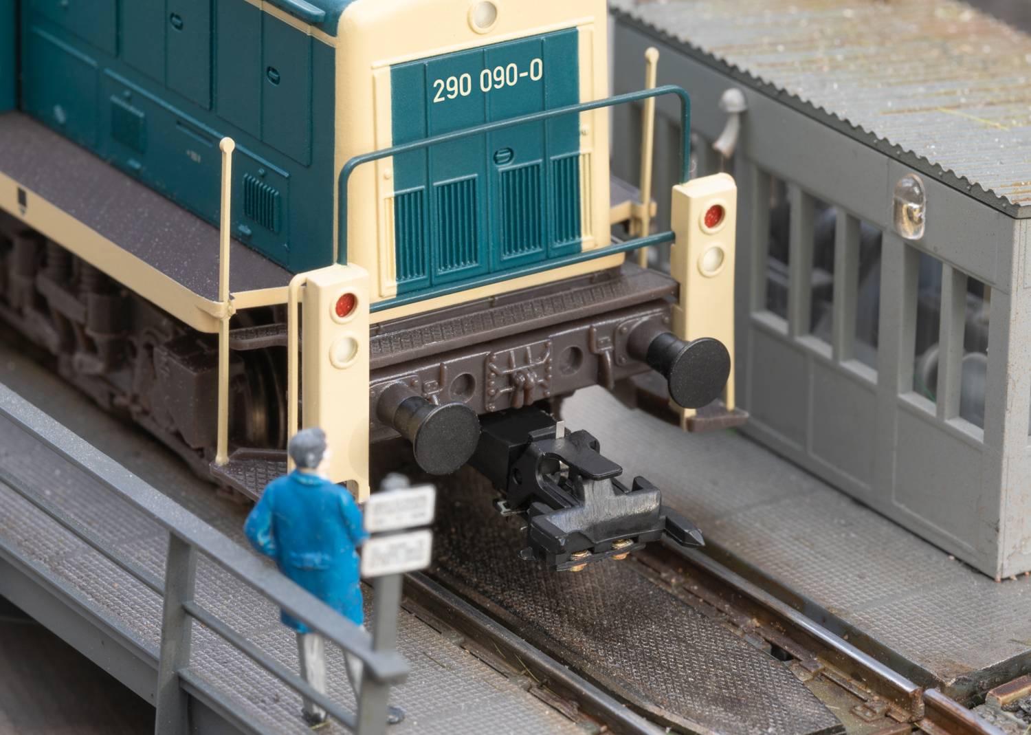 Een modelspoorbaan-locomotief in blauw-witte kleur op een spoor. Een modelfiguur in blauwe kleding observeert de scène.