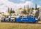 Een modeltreintje met een blauwe locomotief trekt drie zwarte tankwagons langs een landschapsachtergrond met bomen en rotsen.