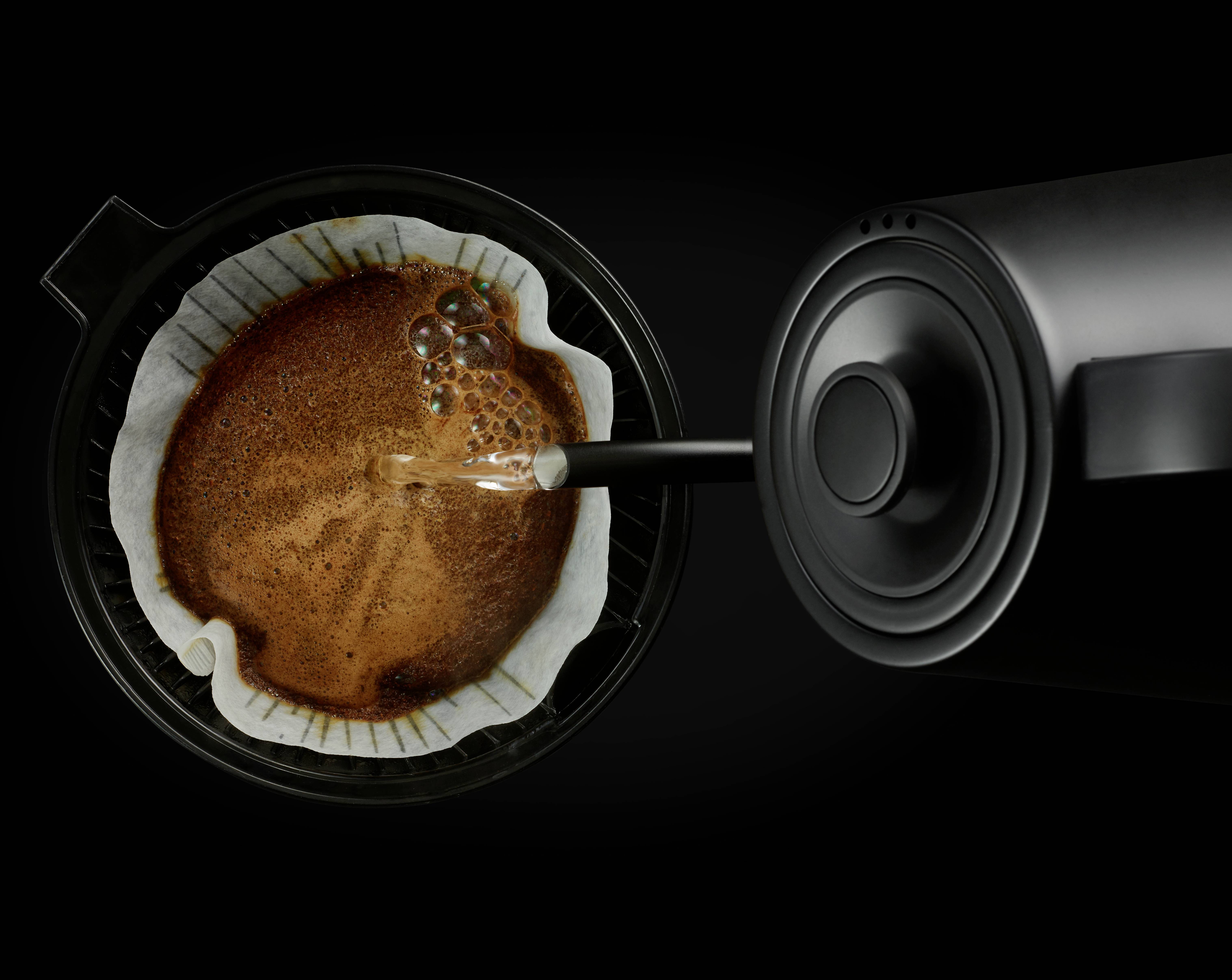 Water wordt uit een zwarte waterkoker over filterkoffie in een koffiemachine gegoten.