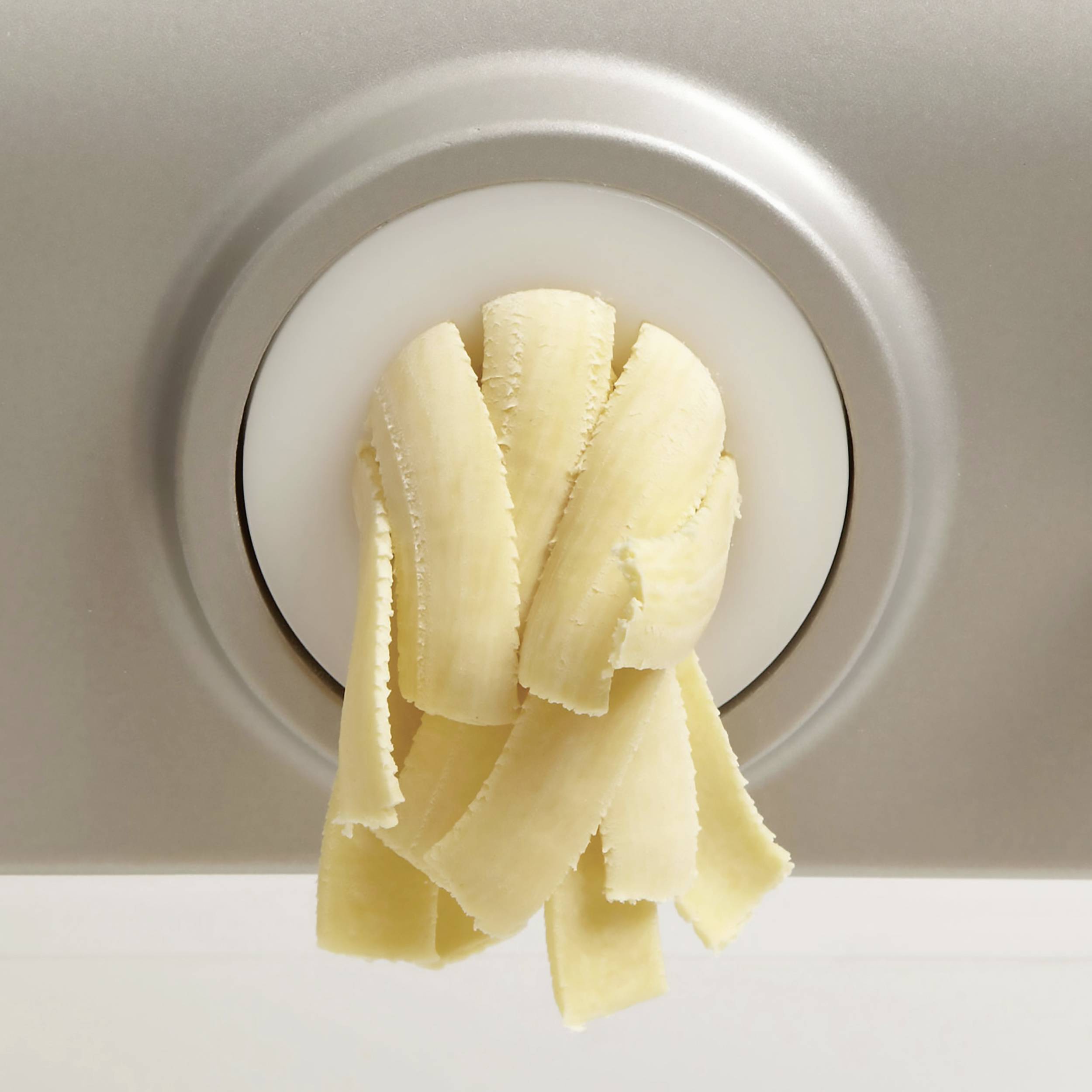 Een spätzle-schaaf drukt deeg door gaatjes om verse spätzle-noedels te maken. De focus ligt op de noedels die uit het apparaat komen.