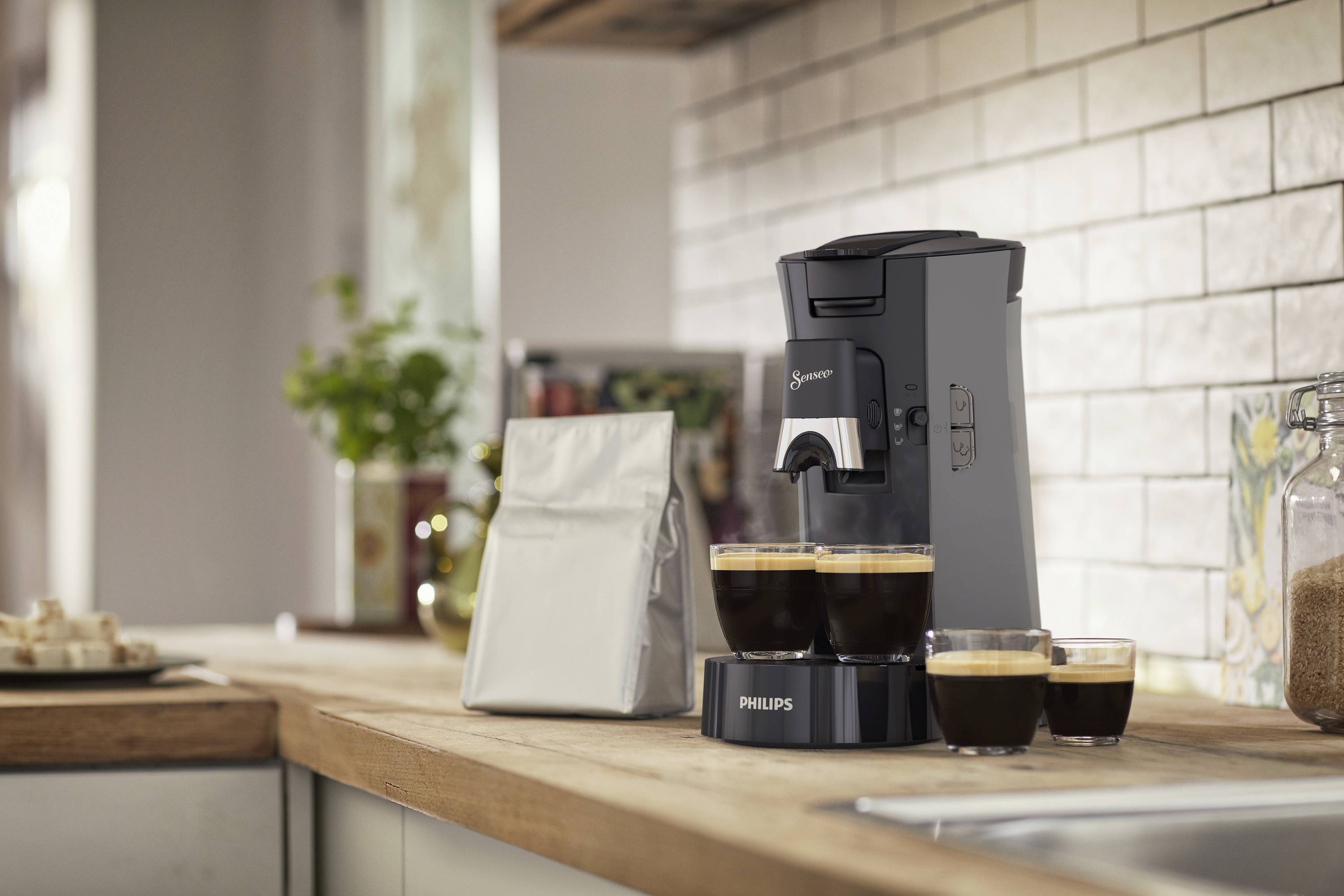 Keukentoonbank met koffiemachine en drie gevulde kopjes, naast een zak koffie. Ontspannen, uitnodigende sfeer.