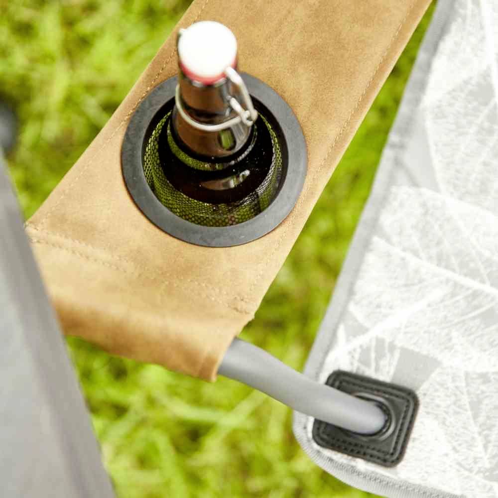 Fles met beugelsluiting in een bekerhouder van een campingstoel, geplaatst op een groene weide.