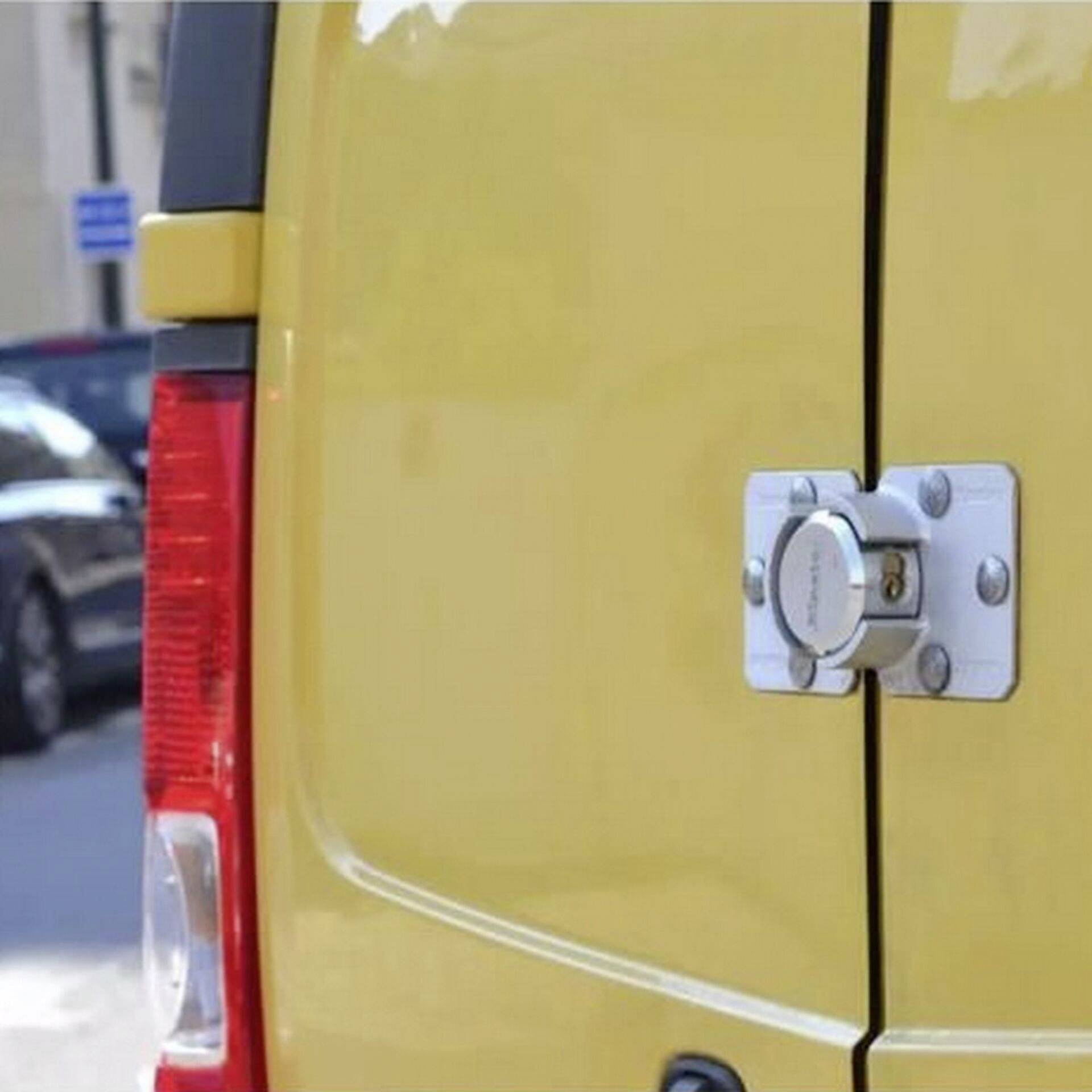 Een gele bestelwagen met een gesloten slot op de achterdeur, geparkeerd op een straat bij daglicht.