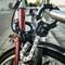 Een rode fiets is vergrendeld met een stevig U-slot aan een metalen leuning. Personen zijn wazig zichtbaar op de achtergrond.