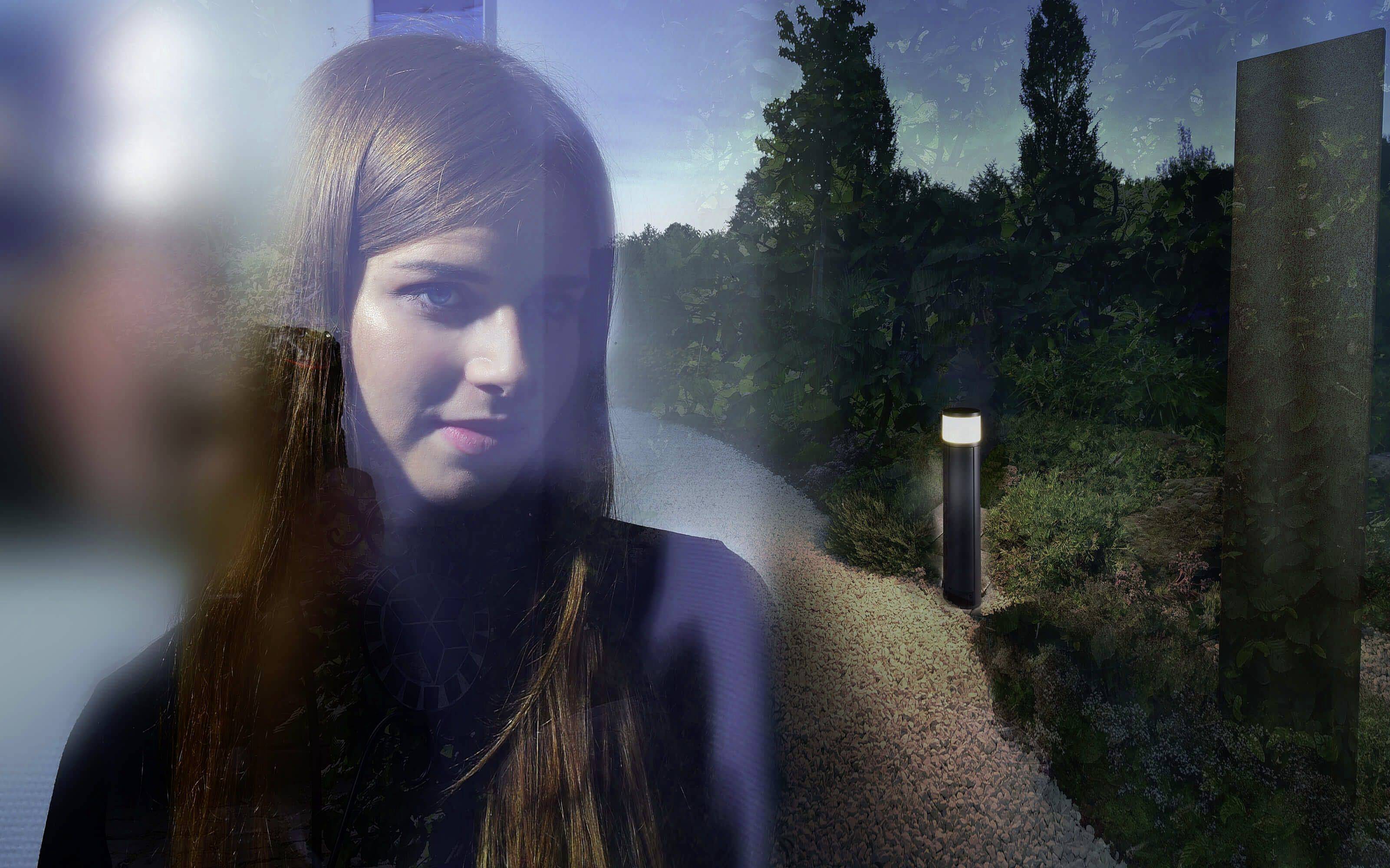 Een vrouw met lang haar staat voor een nachtelijk landschap met een verlicht pad en bomen op de achtergrond.