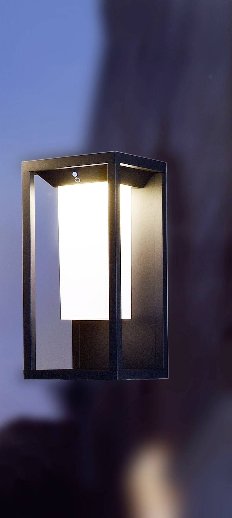 Moderne wandlamp met rechthoekig frame en helder, diffuus licht. Hij hangt aan een gladde muur bij het invallen van de avond.