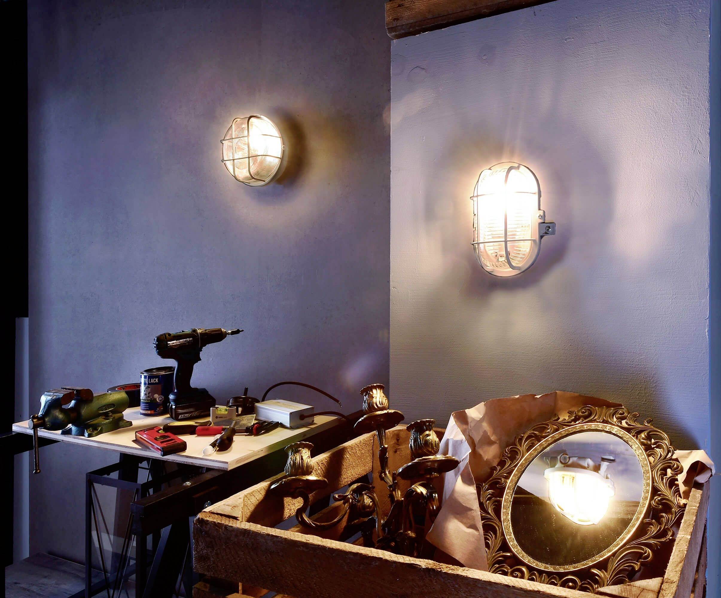 Een ruimte met gedempt licht, links een tafel met gereedschappen en boormachine, rechts een spiegel in een houten kist, twee wandlampen.