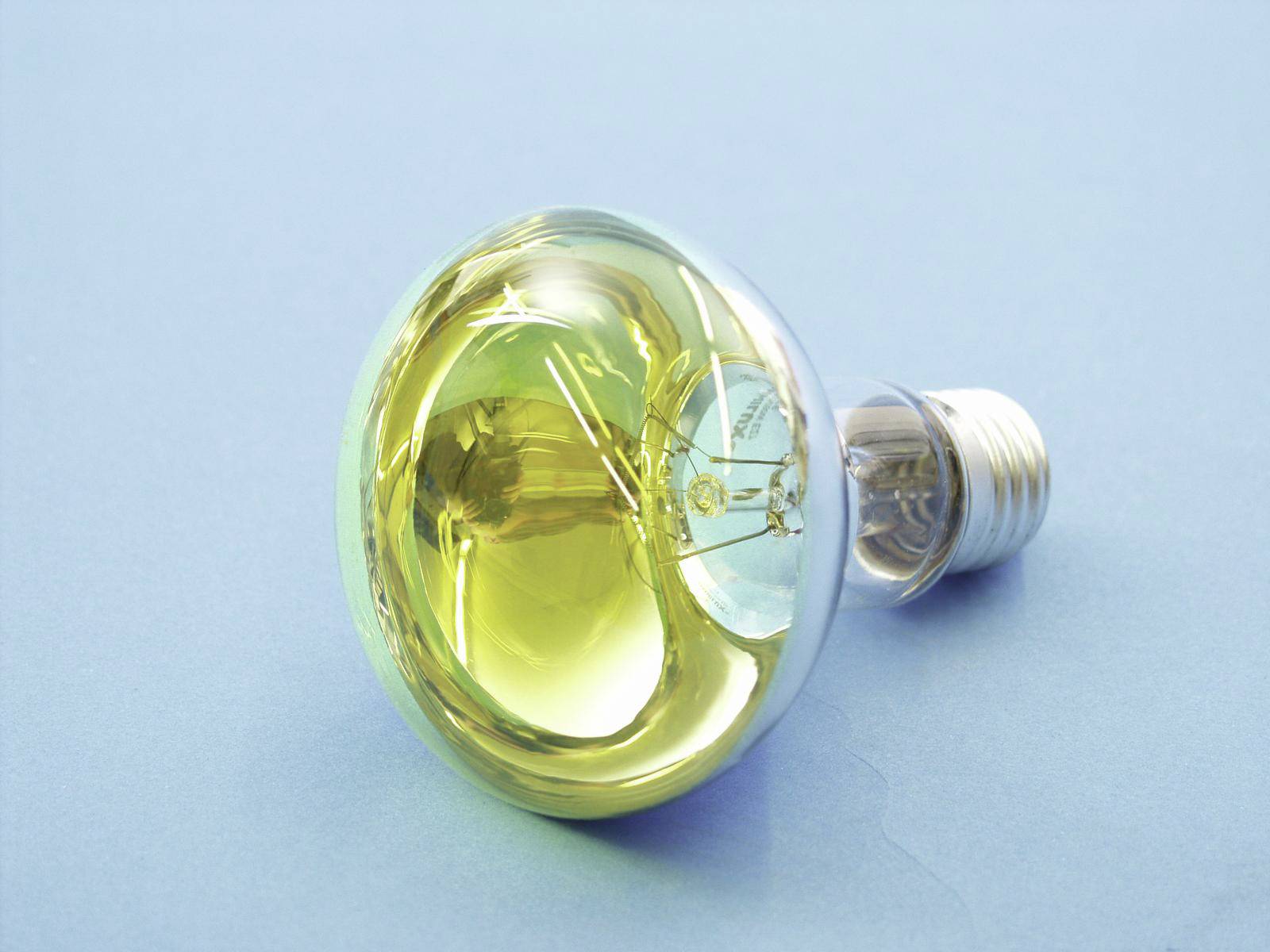Gloeilamp met blauwe en gele glans, liggend op een lichtblauwe ondergrond.
