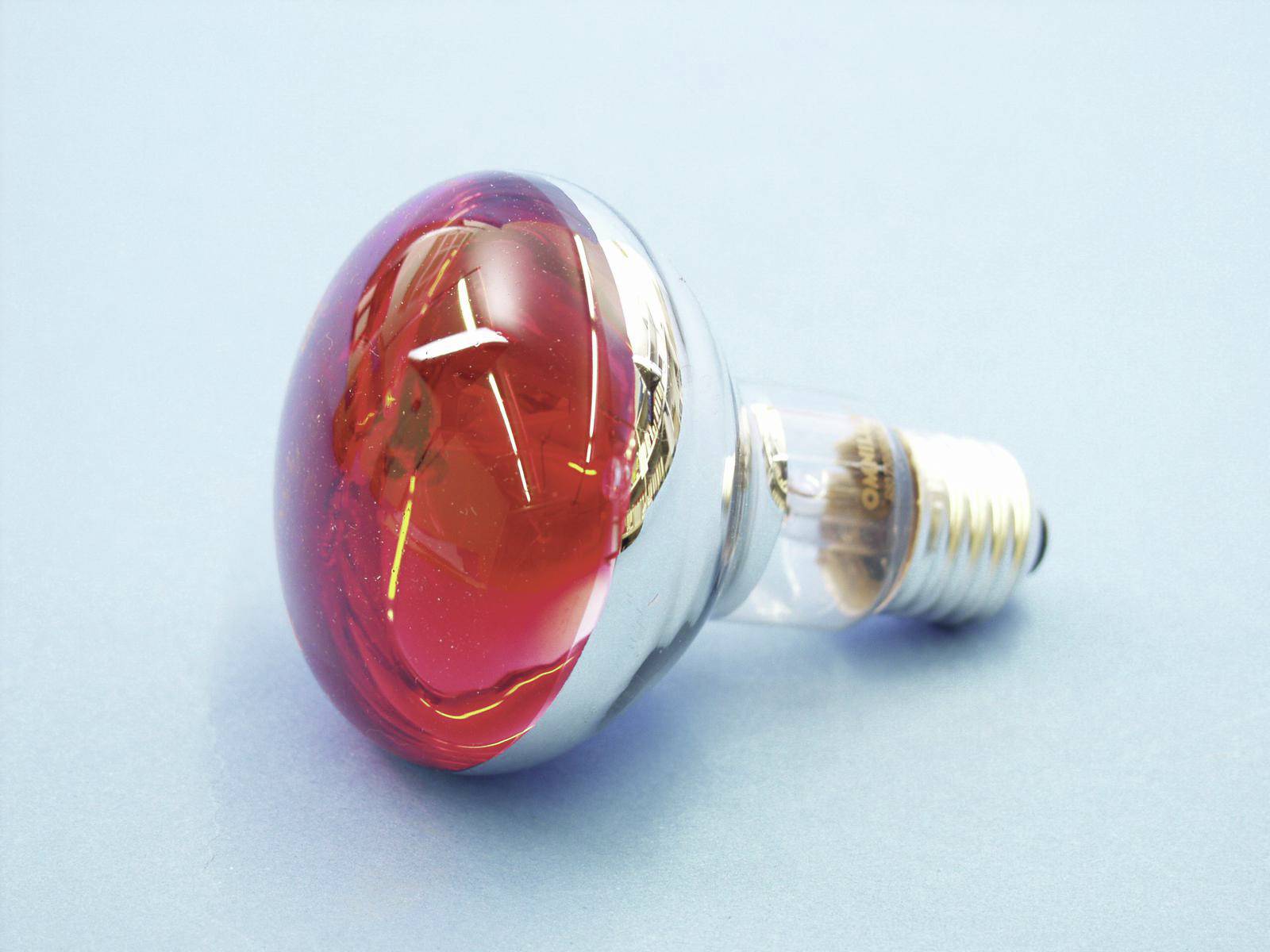 Gloeilamp met rode glazen bol en zilveren fitting op lichtblauwe achtergrond.