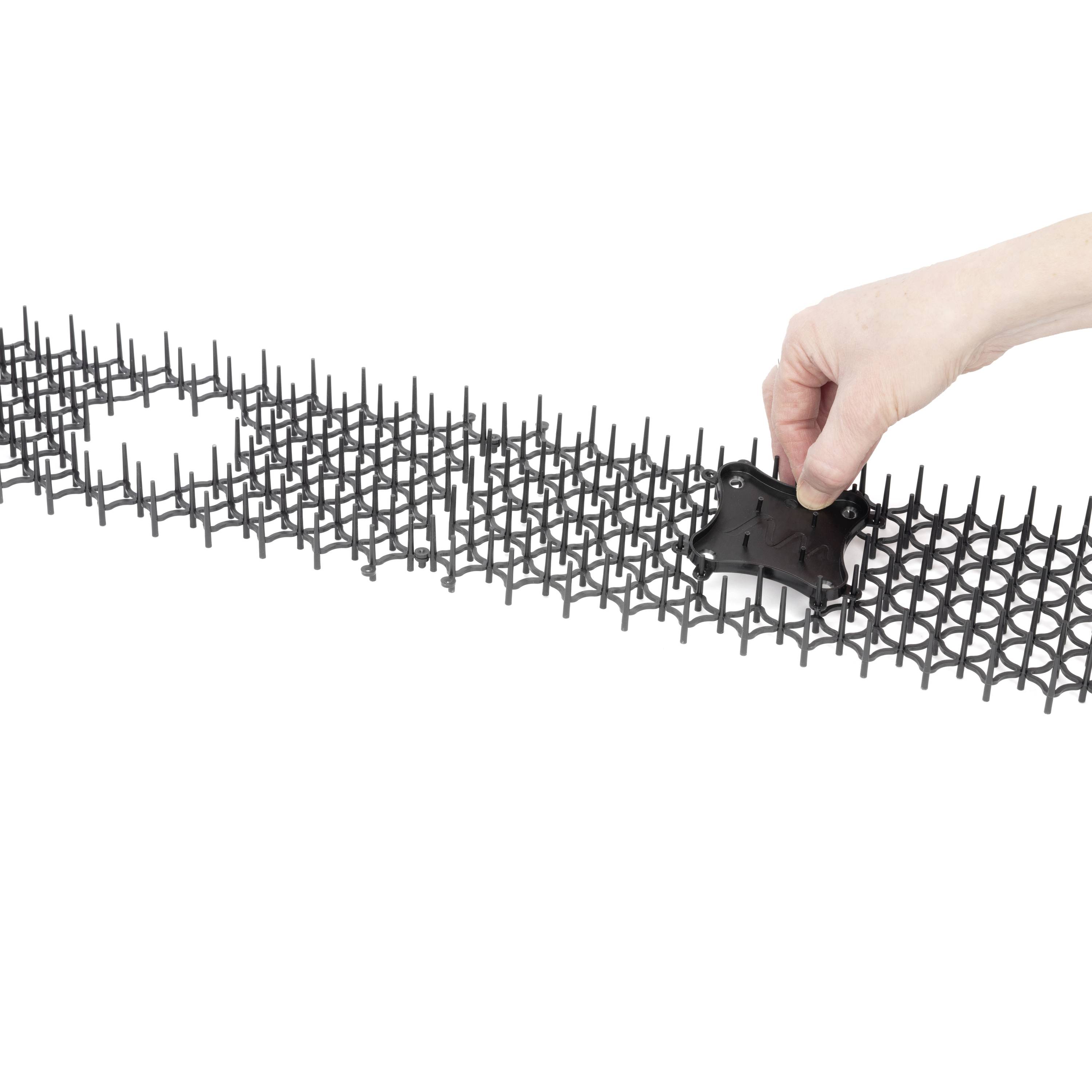 Een hand plaatst een enkel zwart onderdeel in een rasterstructuur. De structuur lijkt modulair en uitbreidbaar te zijn.