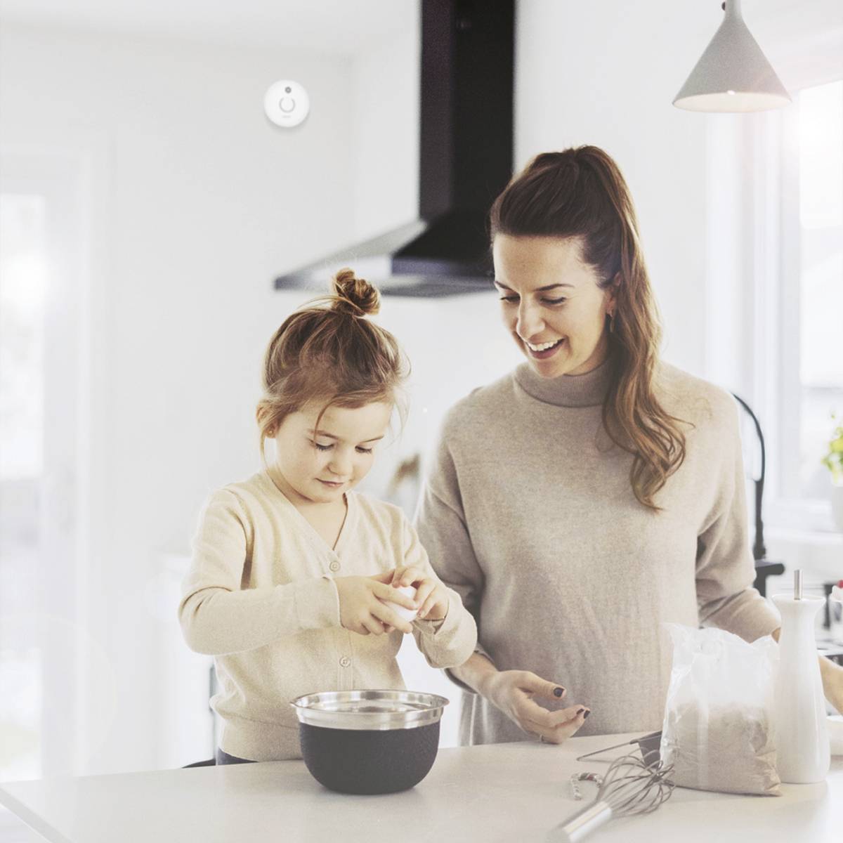 Vrouw en kind bakken samen in een lichte keuken. Beiden glimlachen en het kind vult een kom met ingrediënten.