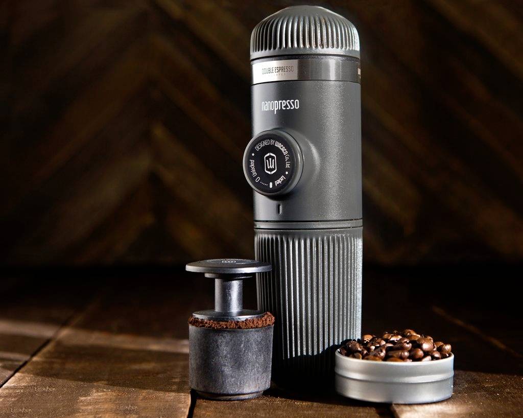 Draagbare espressomachine op een houten tafel, omringd door gemalen koffie en koffiebonen; ideaal voor reizen en kamperen.