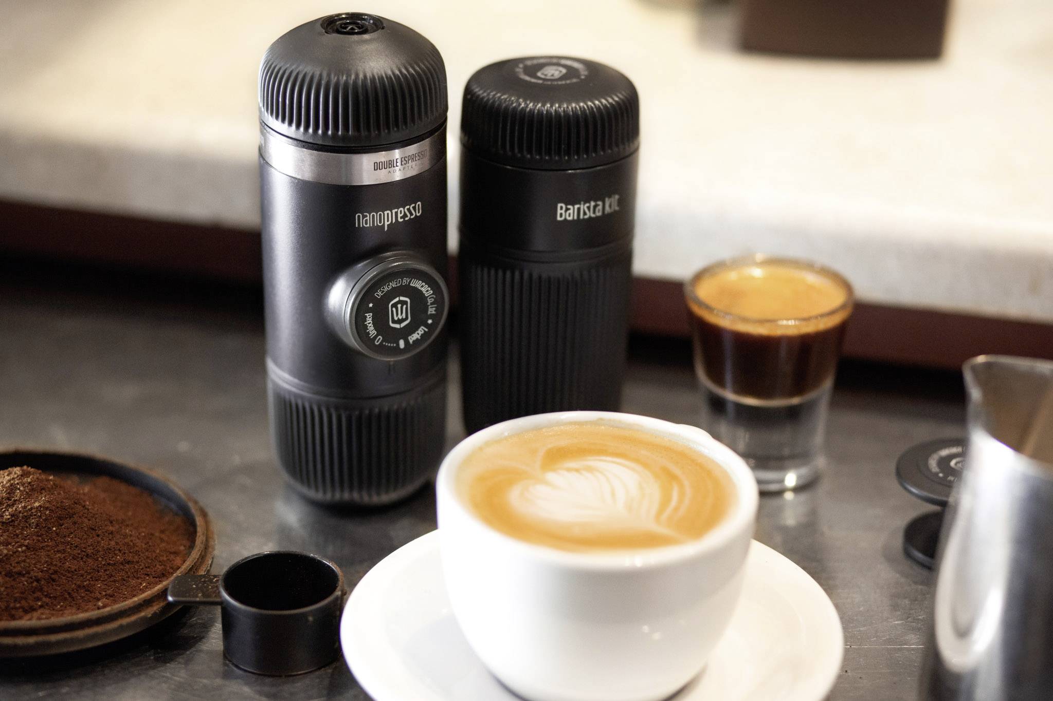 Een draagbare espressomachine staat naast vers gezette koffie en koffiepoeder op een tafel, klaar voor gebruik.