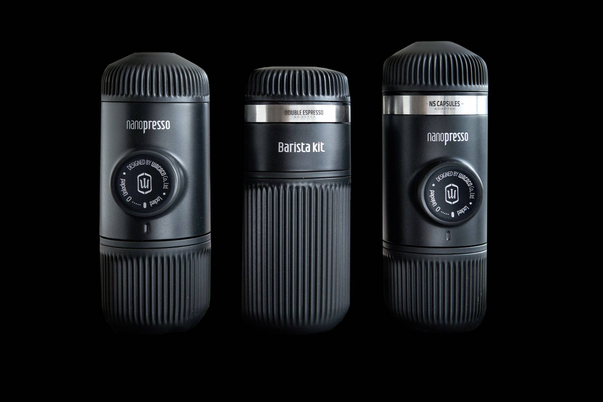Drie draagbare koffiemachines in het zwart op een zwarte achtergrond. Links en rechts elk een 'Nanopresso', in het midden een 'Barista Kit'.