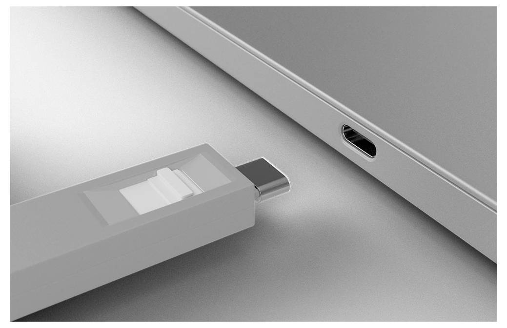USB-flashstation ingeplugd in een laptoppoort van USB-C, weergegeven in close-up op een grijs oppervlak.