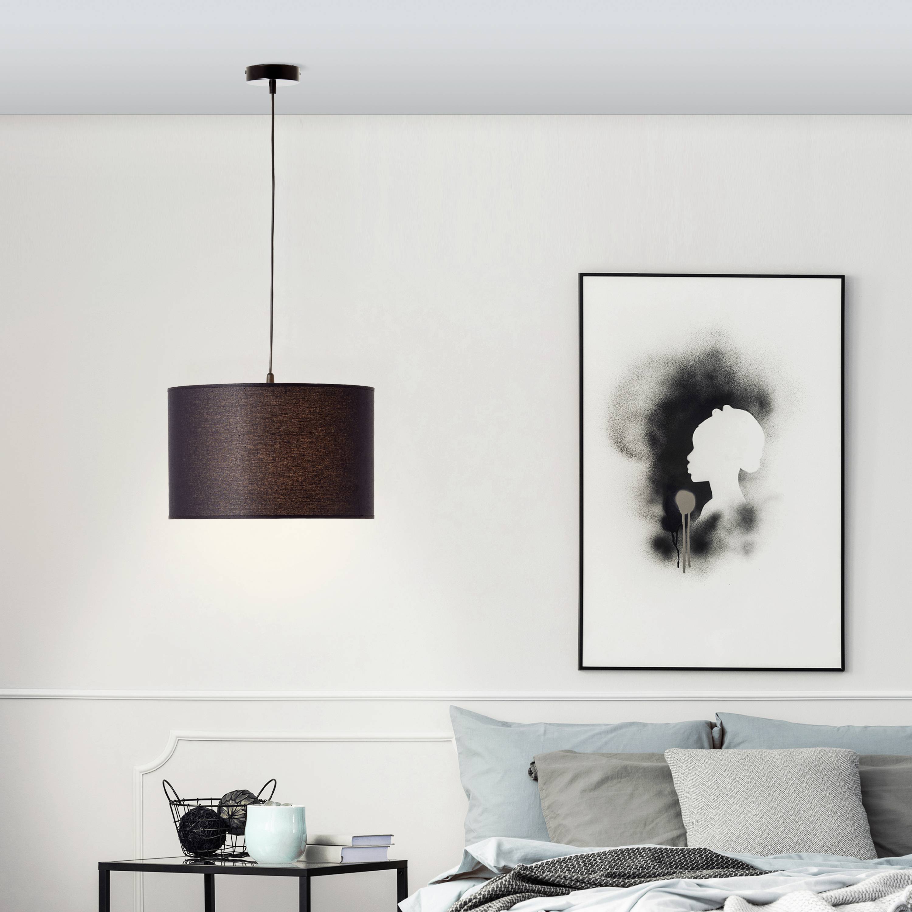 Woonkamer met hangende lamp, stijlvol kunstwerk aan de muur, bank met grijze kussens en een kleine zwarte bijzettafel.