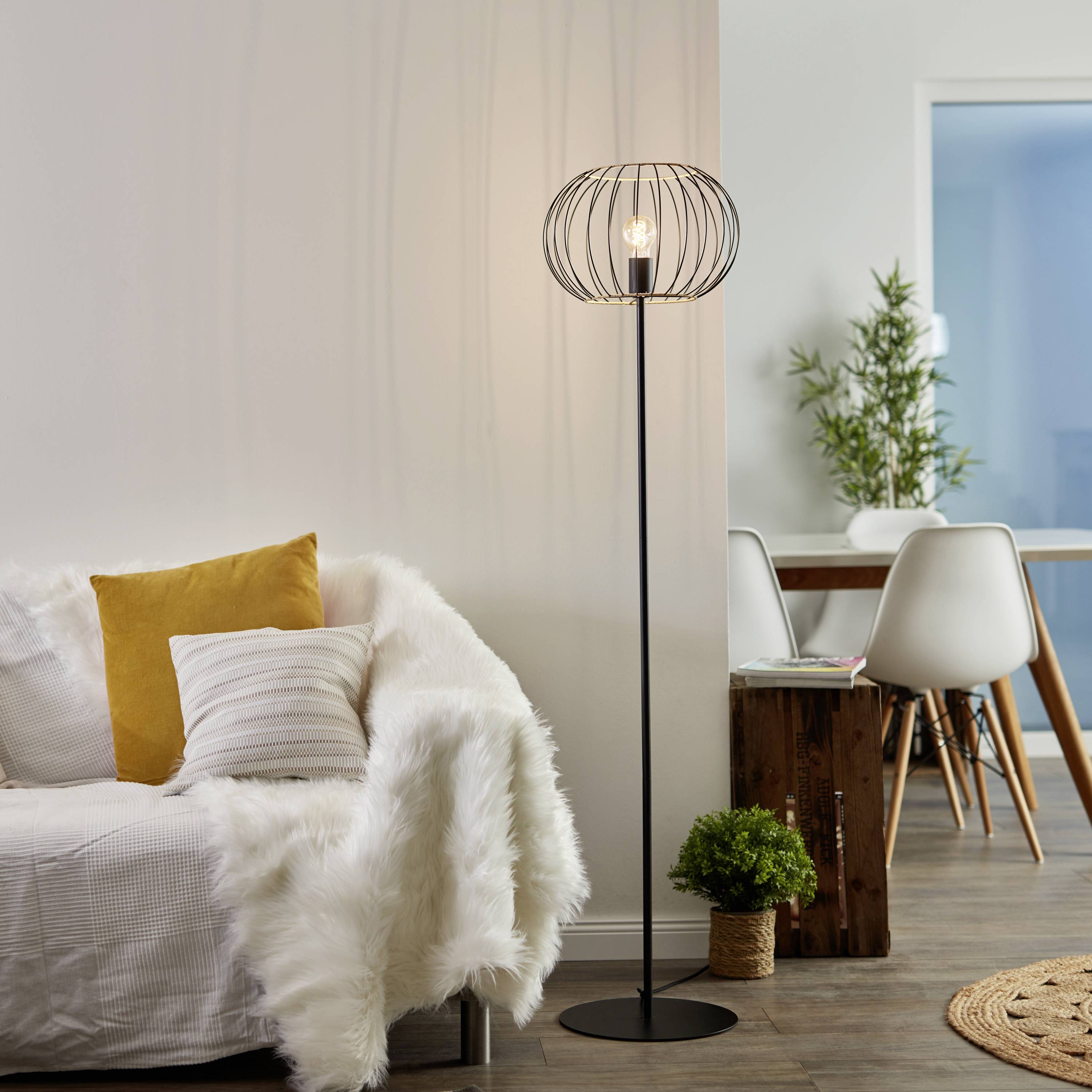 Een gezellige woonkamer met een bank, geflankeerd door een moderne vloerlamp en een eettafel op de achtergrond.