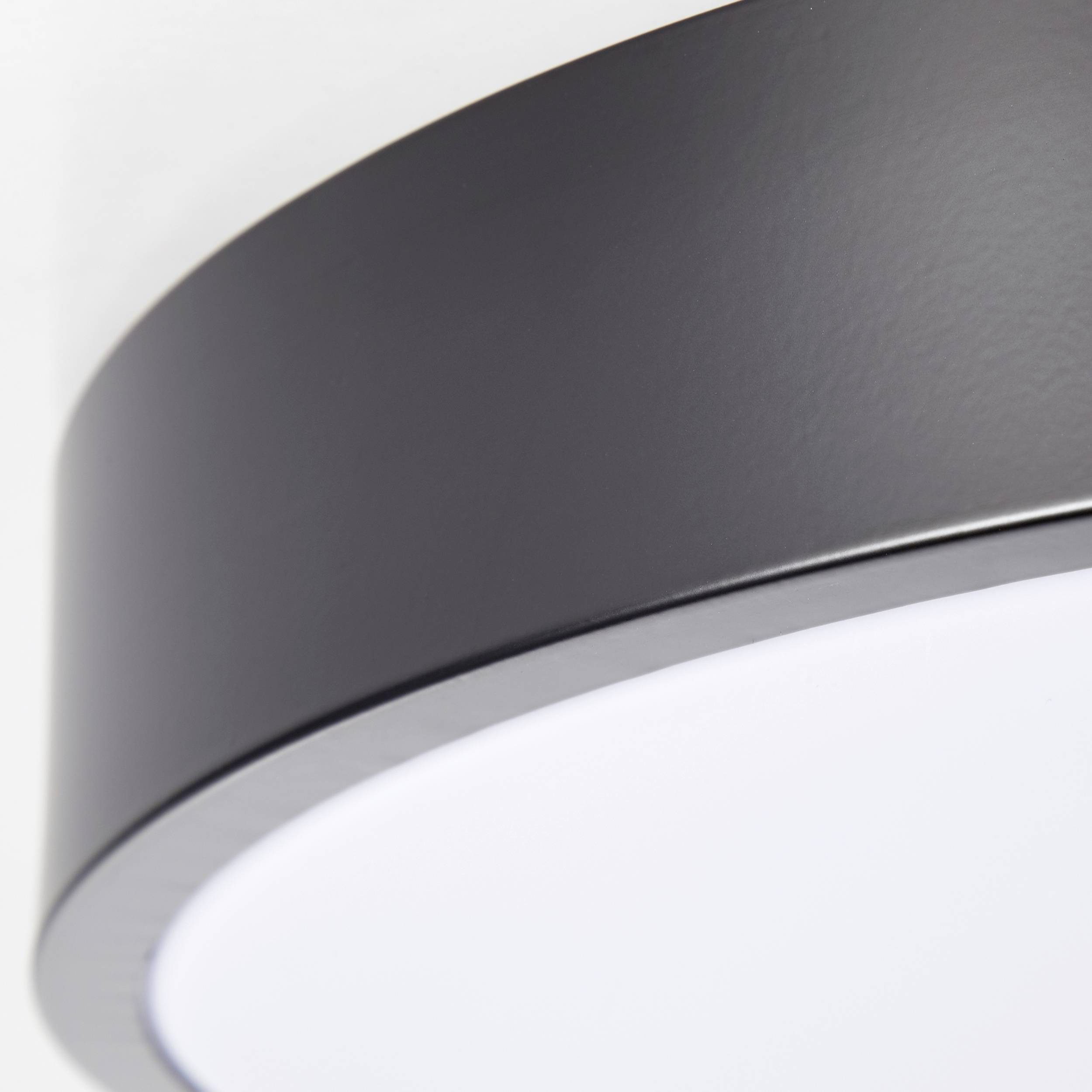 Een moderne, ronde plafondlamp met een strak, zwart frame en een witte lichtoppervlakte.