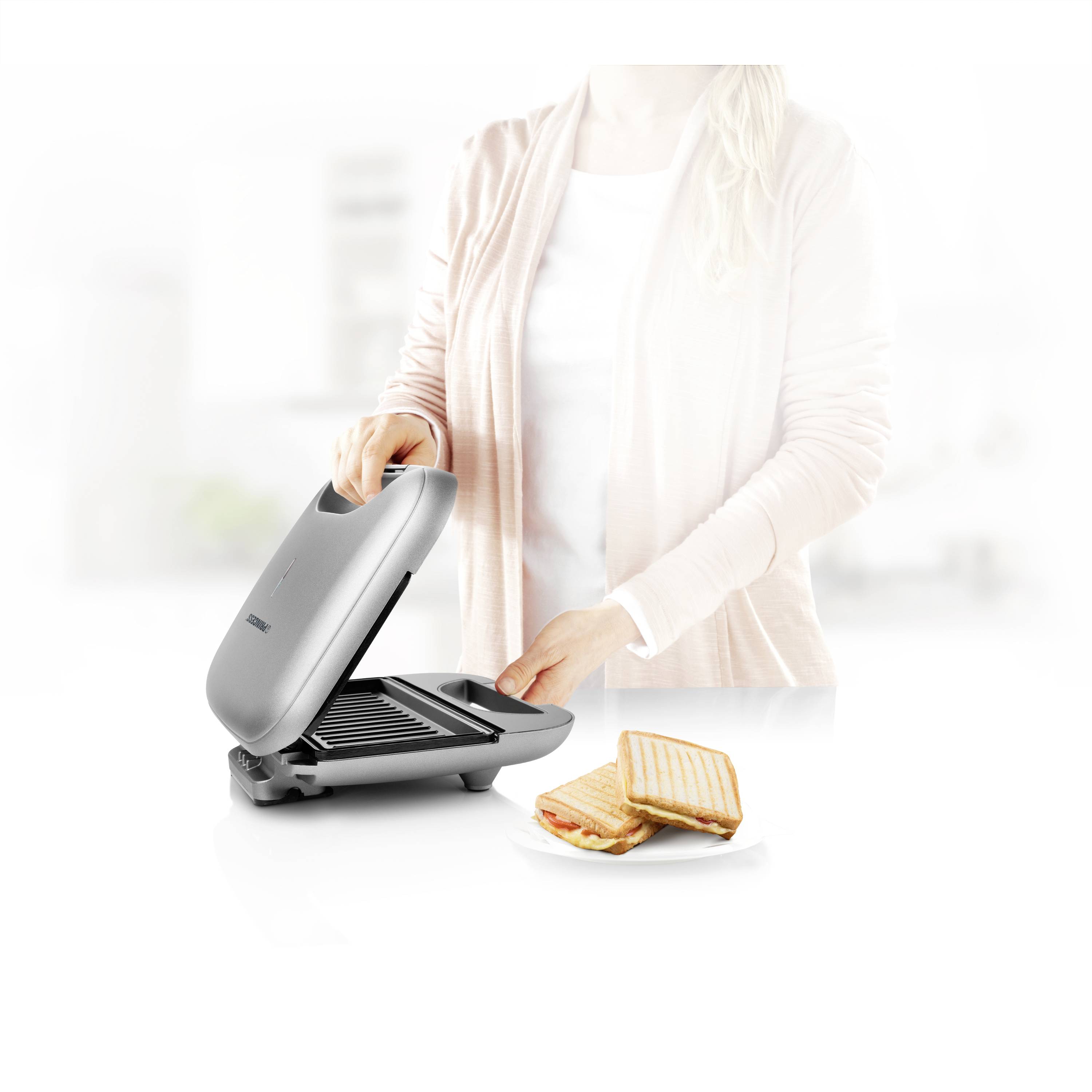 Een persoon gebruikt een tosti-ijzer. Naast hem/haar staat een bord met klaar gemaakte tosti's.