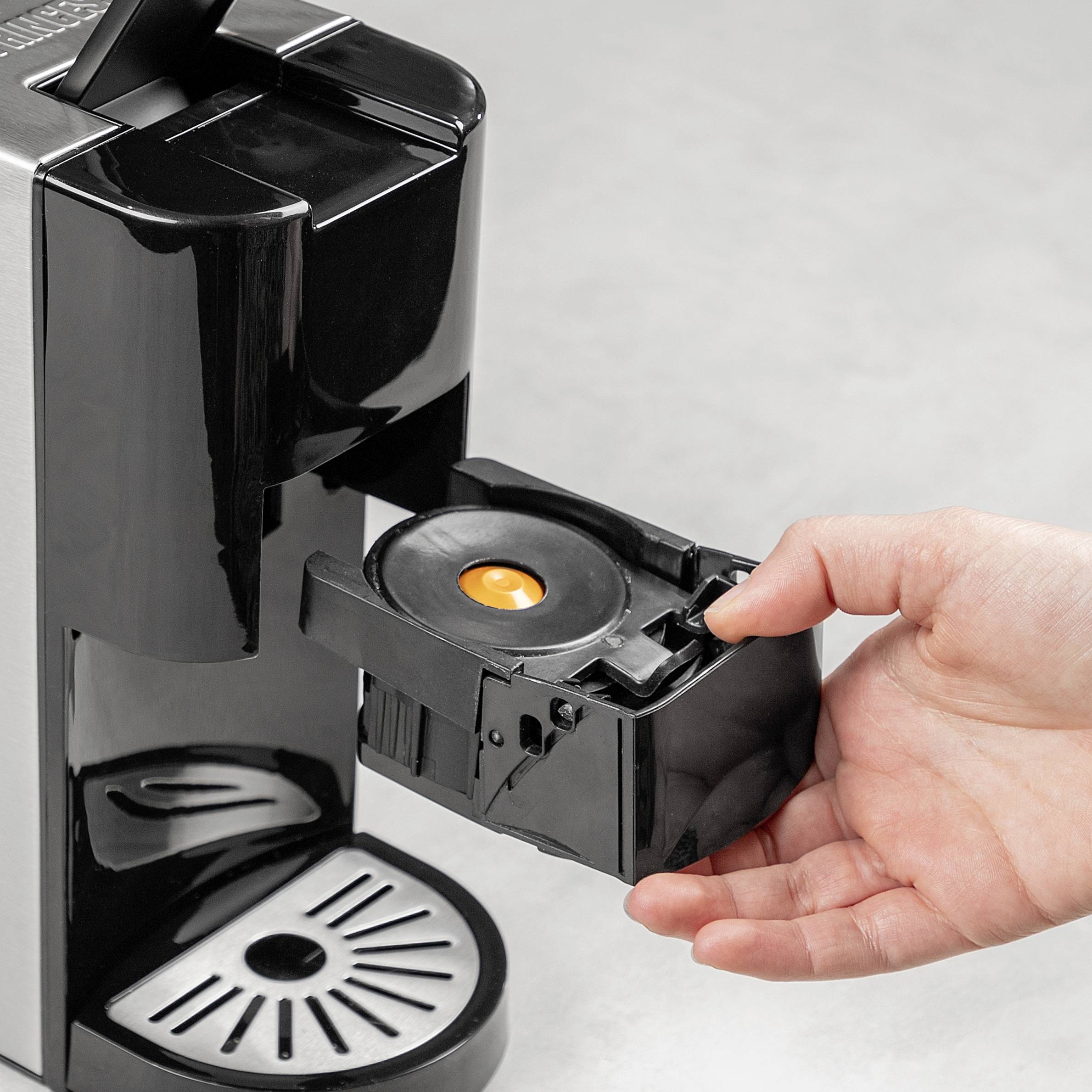 Hand plaatst oranje koffiecapsule in een zwarte capsuleautomaat.