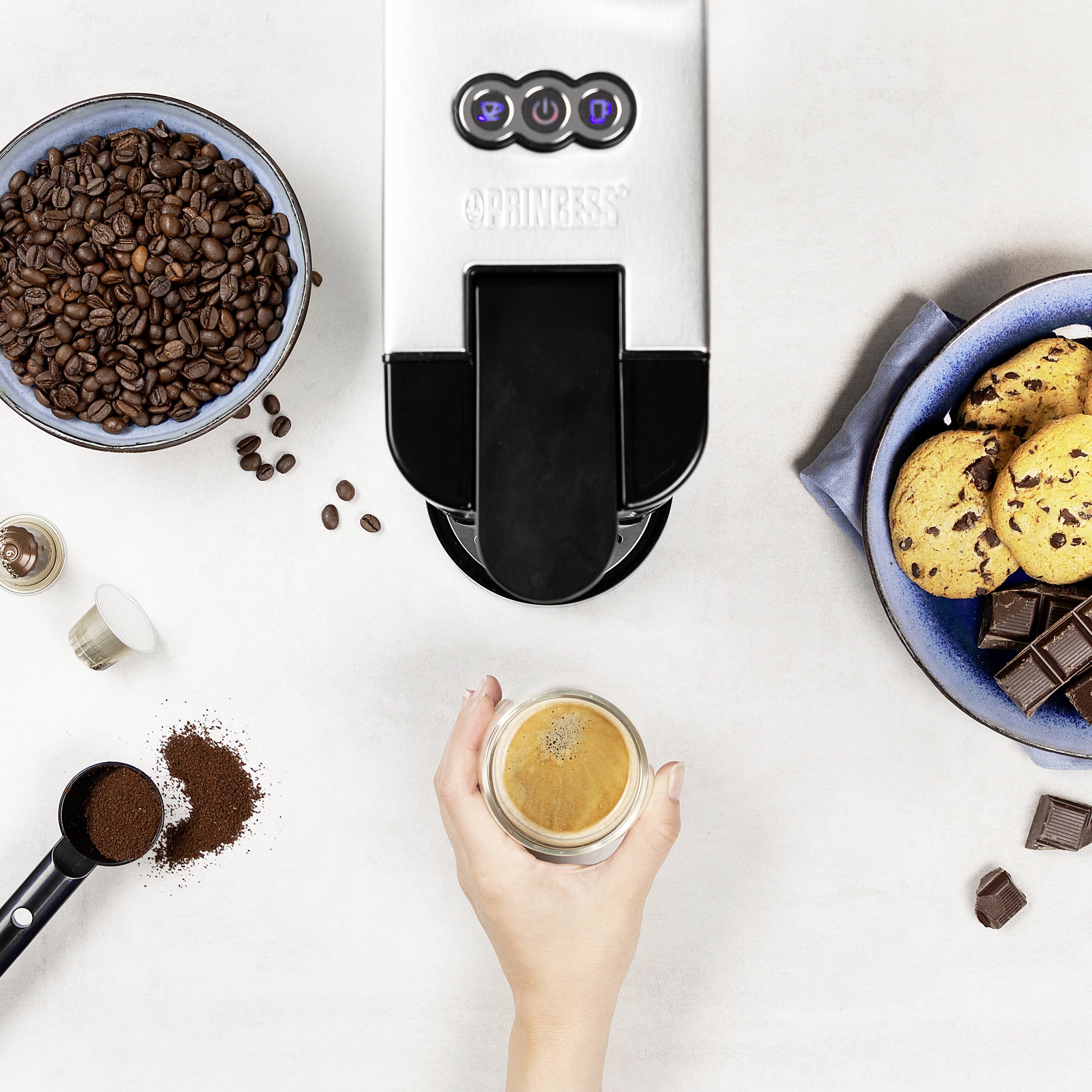 Een hand houdt een kopje espresso onder een koffiemachine. Ernaast zijn koffiebonen, gemalen koffie en koekjes te zien.