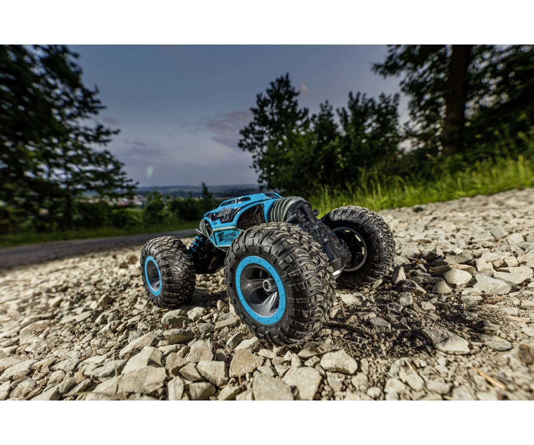 Afstandsbestuurde auto op ruw terrein, met blauwe accenten, rijdt over een rotsachtig pad, omgeven door bomen bij schemering.