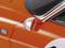 Close-up van een oranje klassieke auto. Zichtbaar is een deel van de bestuurdersdeur met een zilveren zijspiegel.